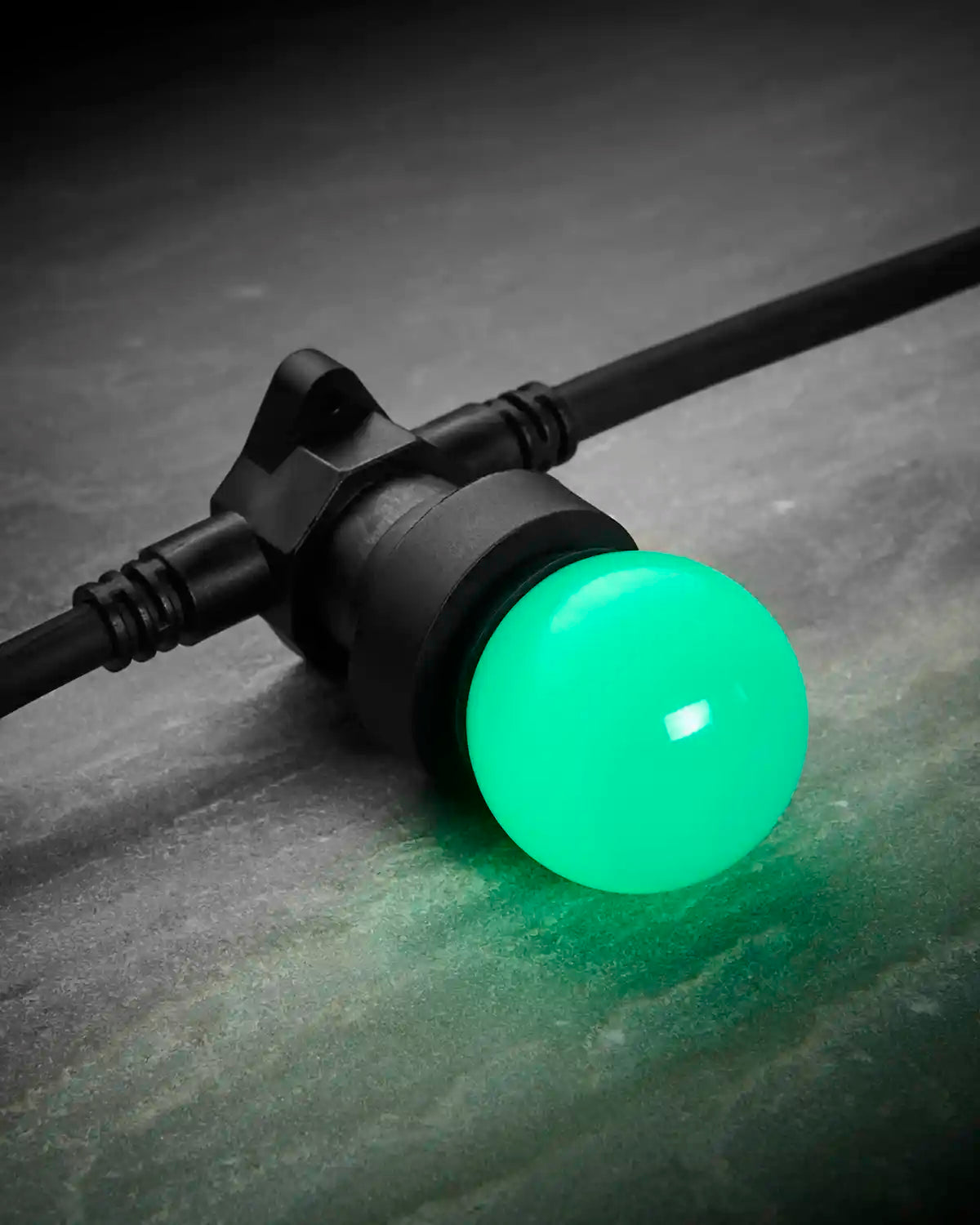 Close-up of a green E27 LED bulb fitted into a black festoon belt on a dark stone-effect surface.
