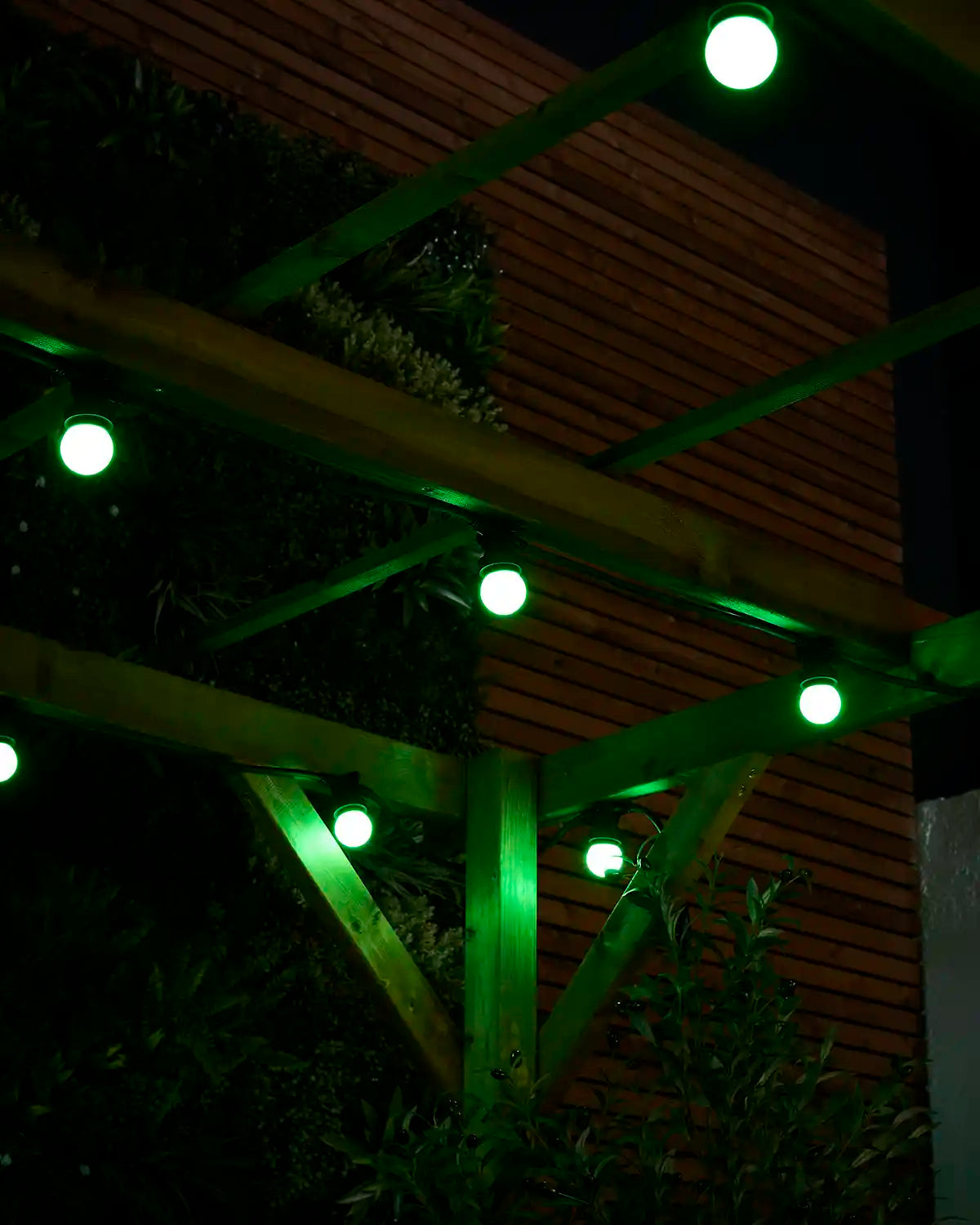 Green E27 festoon bulbs glowing under wooden pergola beams with garden foliage in the background.
