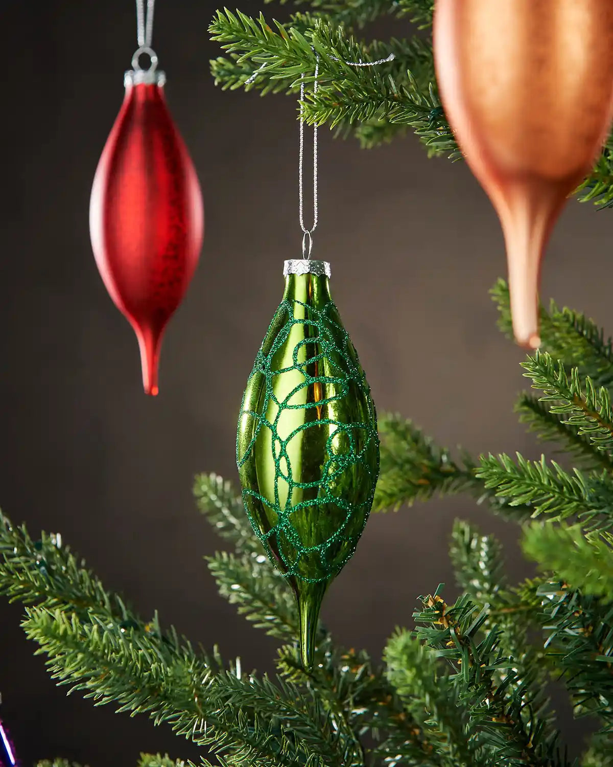 Green glass finial bauble with glitter swirl detail hanging on Christmas tree