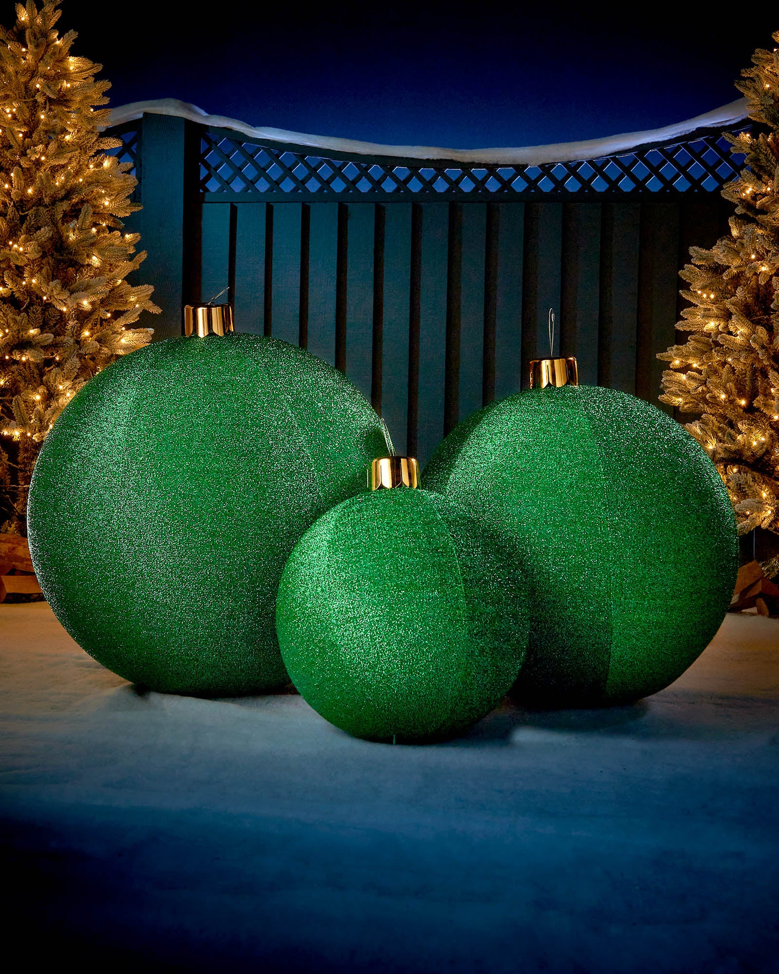 Green inflatable tinsel Christmas baubles in different sizes displayed outdoors with warm festive lights.