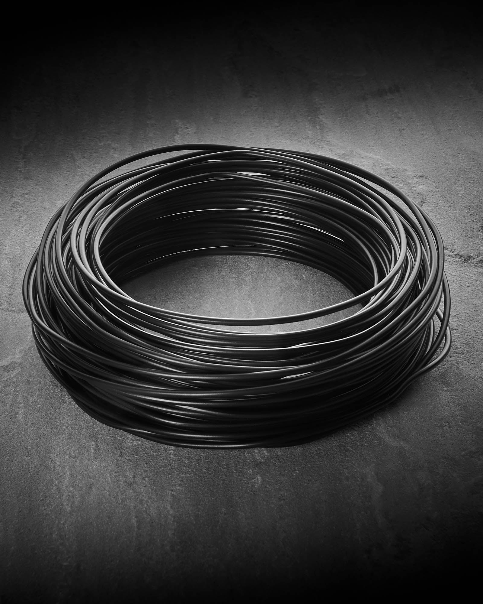 25m heavy duty black catenary cable coiled on a grey surface for supporting festoon lights.