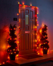 Autumn colour Home Series string lights framing a front door with two lit potted trees.