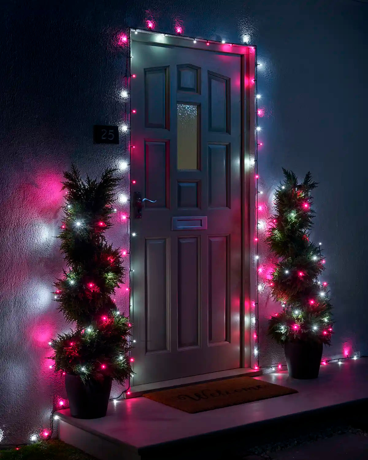 Pink and white Home Series string lights framing a front door with two lit potted trees.