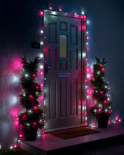 Pink and white Home Series string lights framing a front door with two lit potted trees.