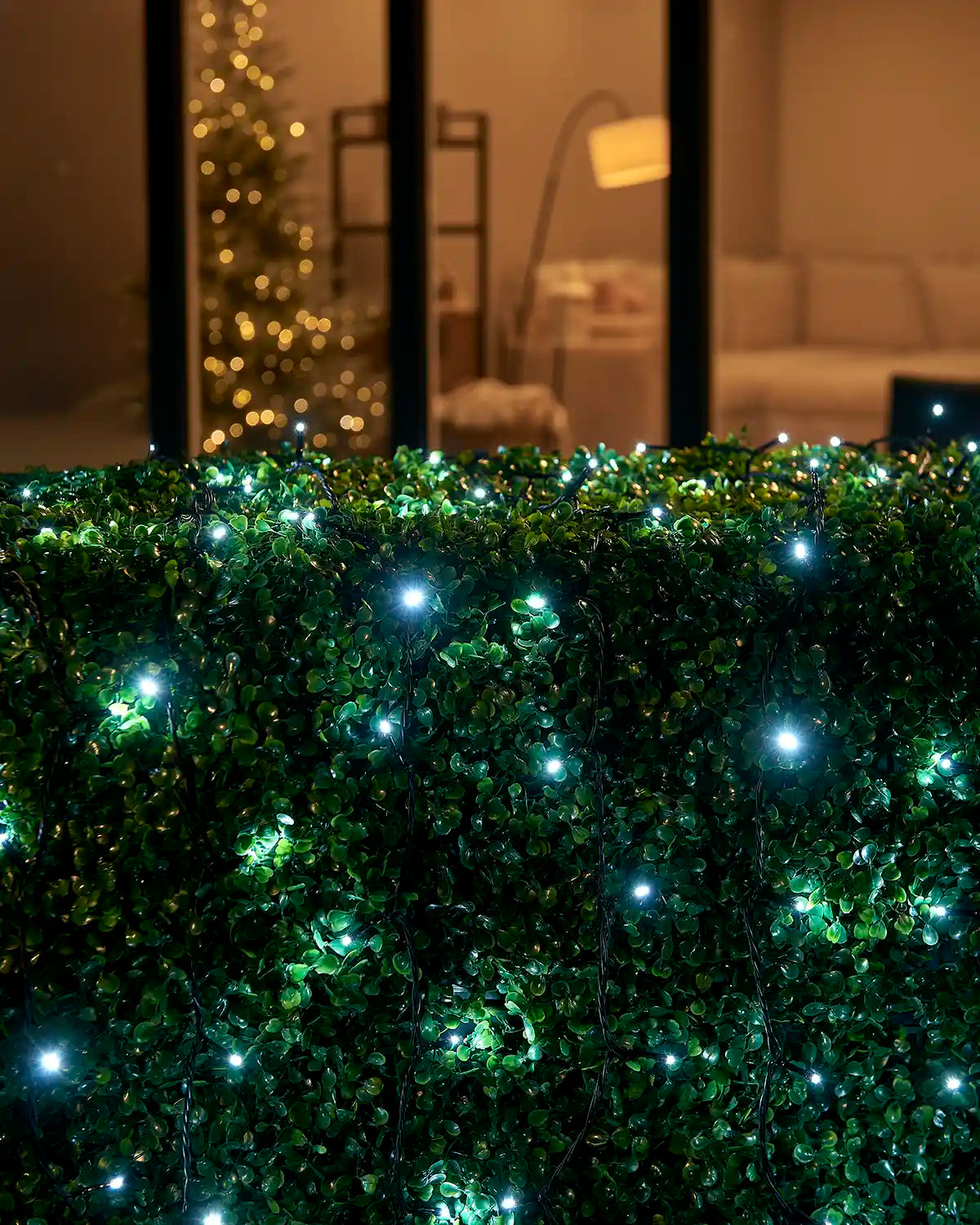 White Home Series string lights arranged across an outdoor hedge by patio doors.