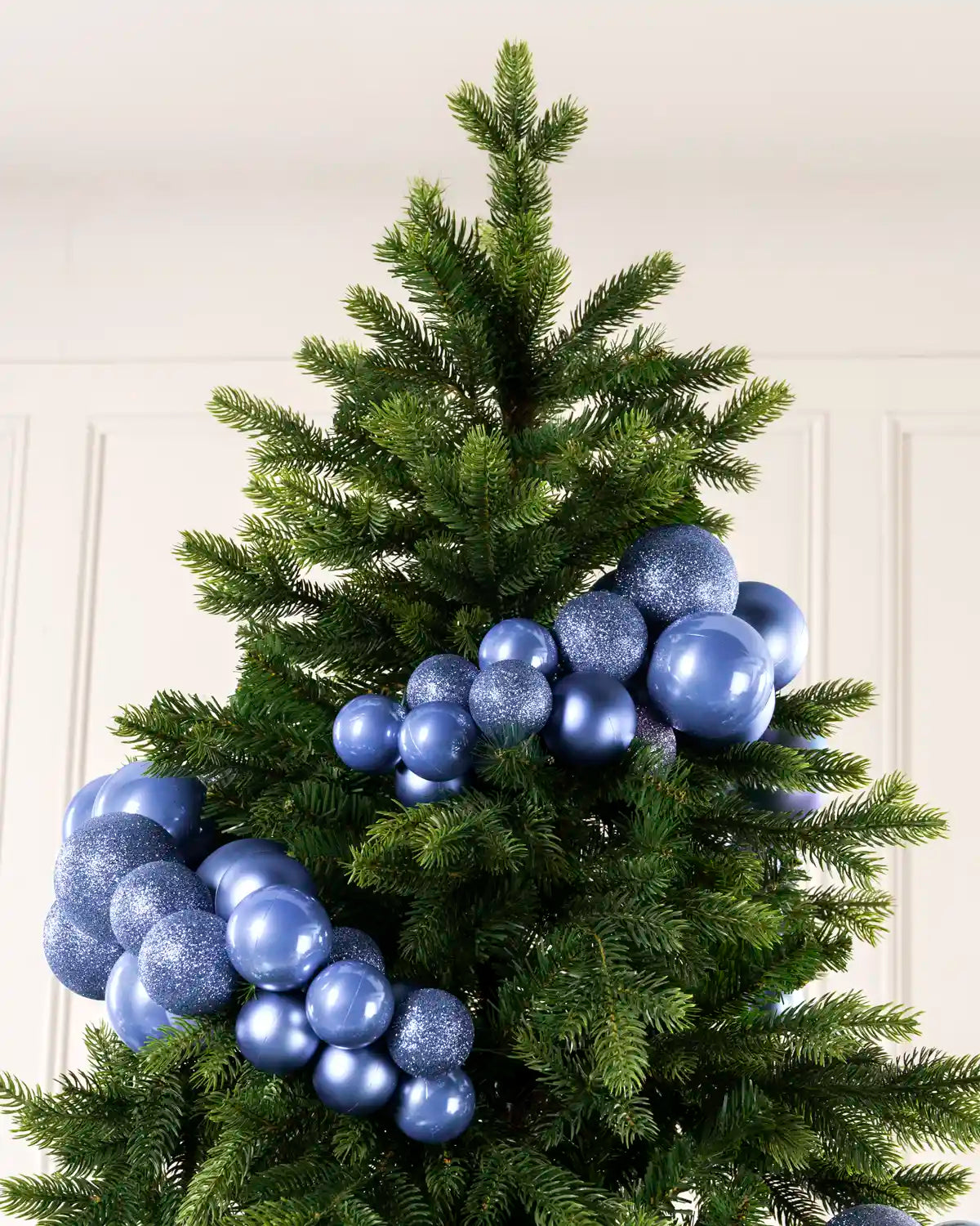 Ice blue bauble cluster arch arranged through the upper branches of a green Christmas tree.