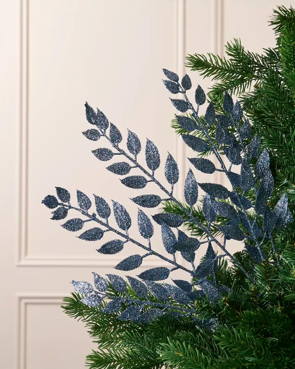 Ice blue leaf Christmas tree spray arranged among green Christmas tree branches.