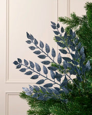 Ice blue leaf Christmas tree spray arranged among green Christmas tree branches.
