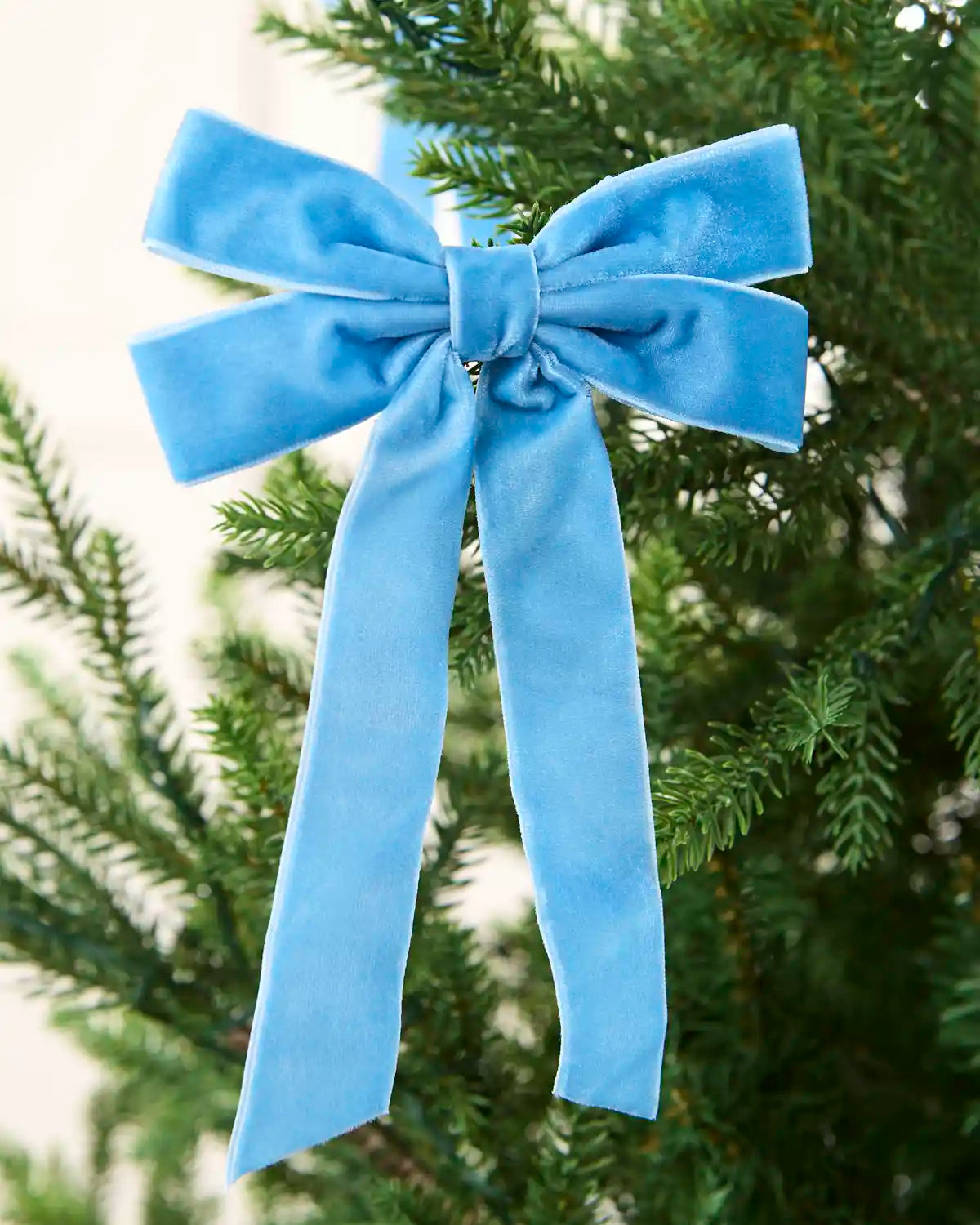 Ice blue 16.5 cm velvet double bow with long tails attached to a Christmas tree branch.