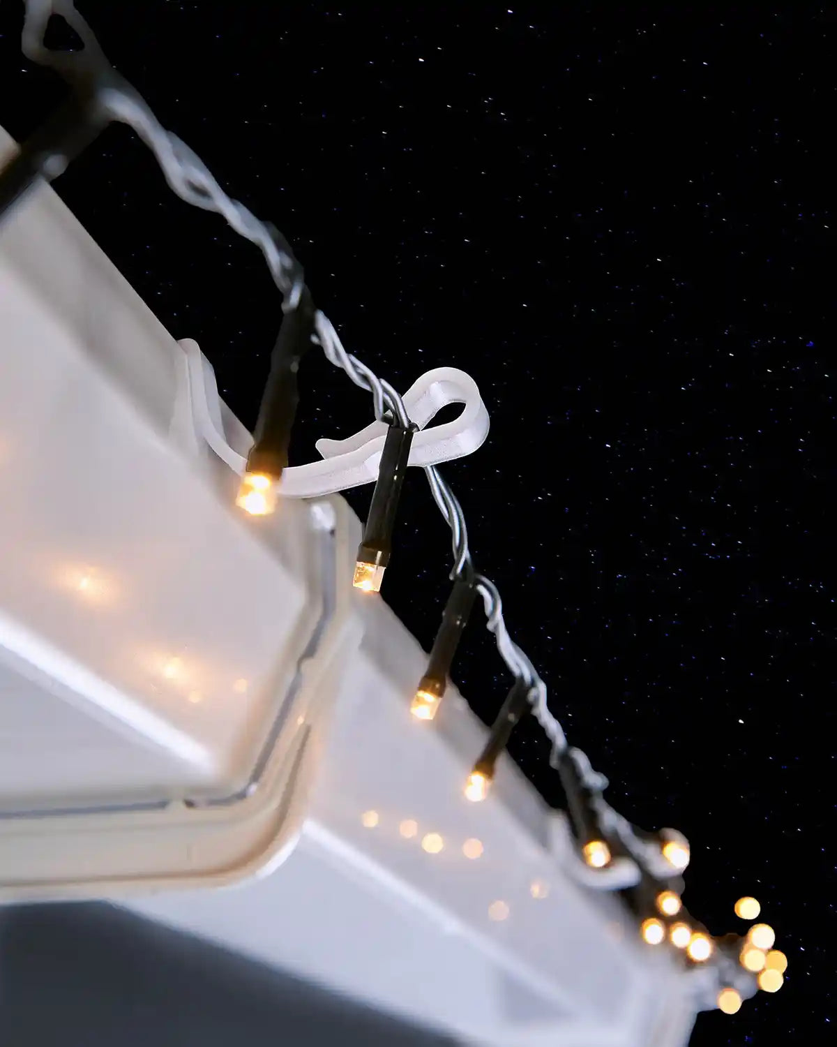 Large gutter hook securing warm white Christmas lights along guttering