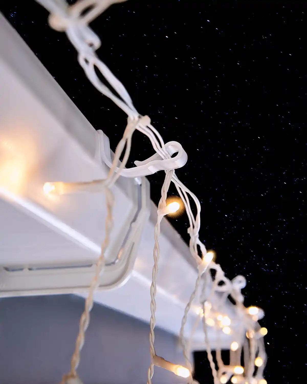 White large gutter hooks holding warm white Christmas lights on guttering