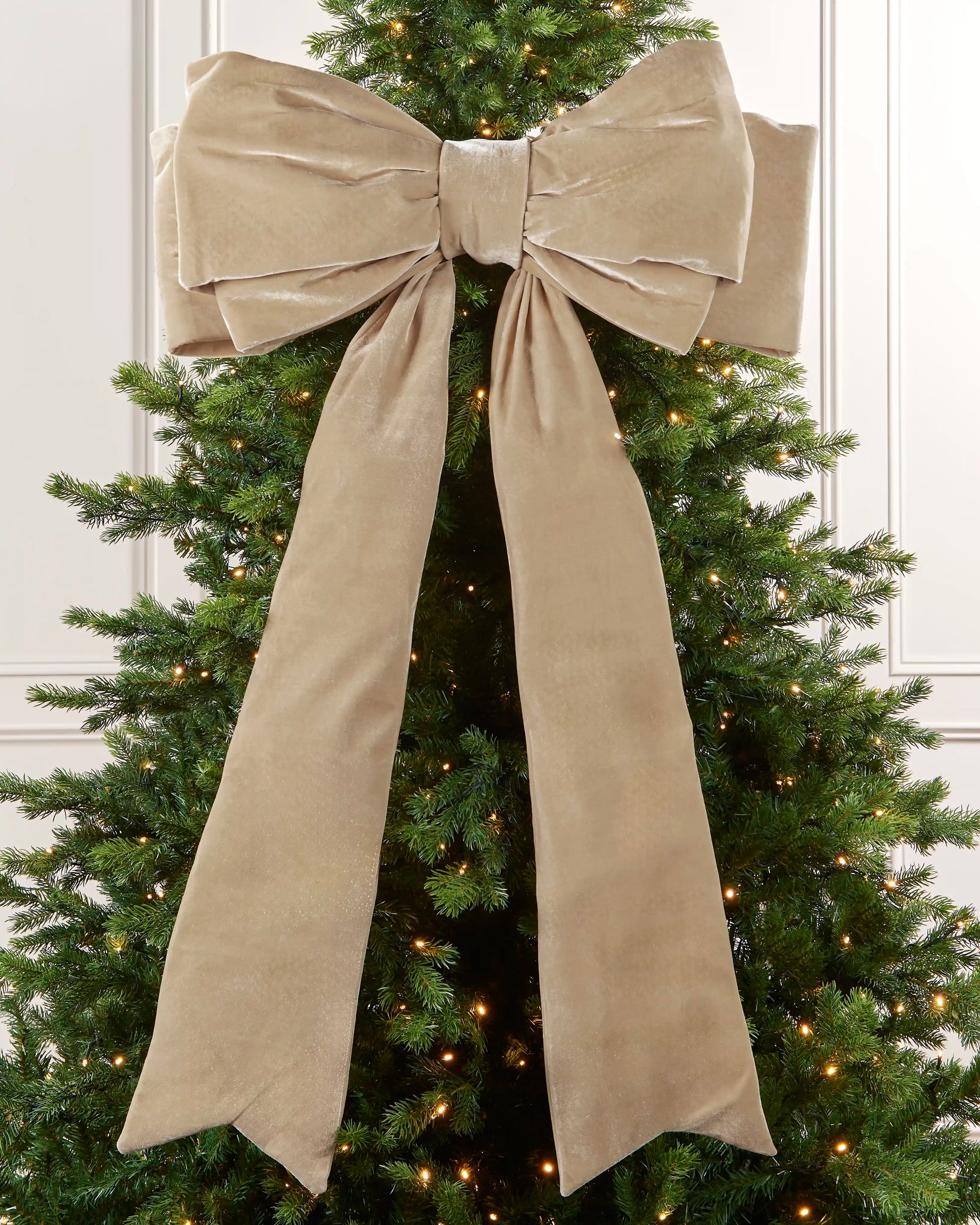 Large 140 cm latte velvet Christmas bow displayed on a lit Christmas tree with long hanging tails.
