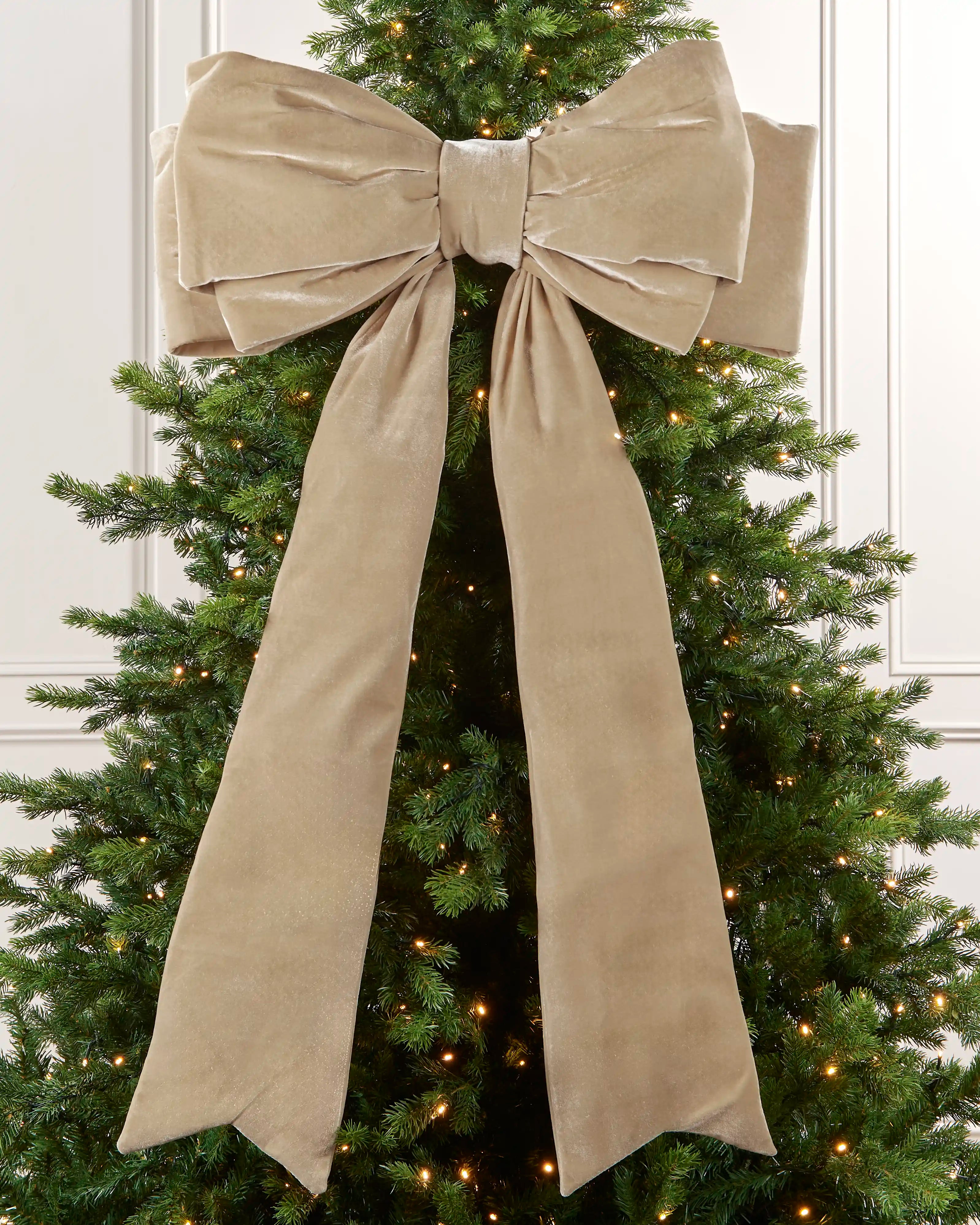 Large 140 cm latte velvet Christmas bow displayed on a lit Christmas tree with long hanging tails.
