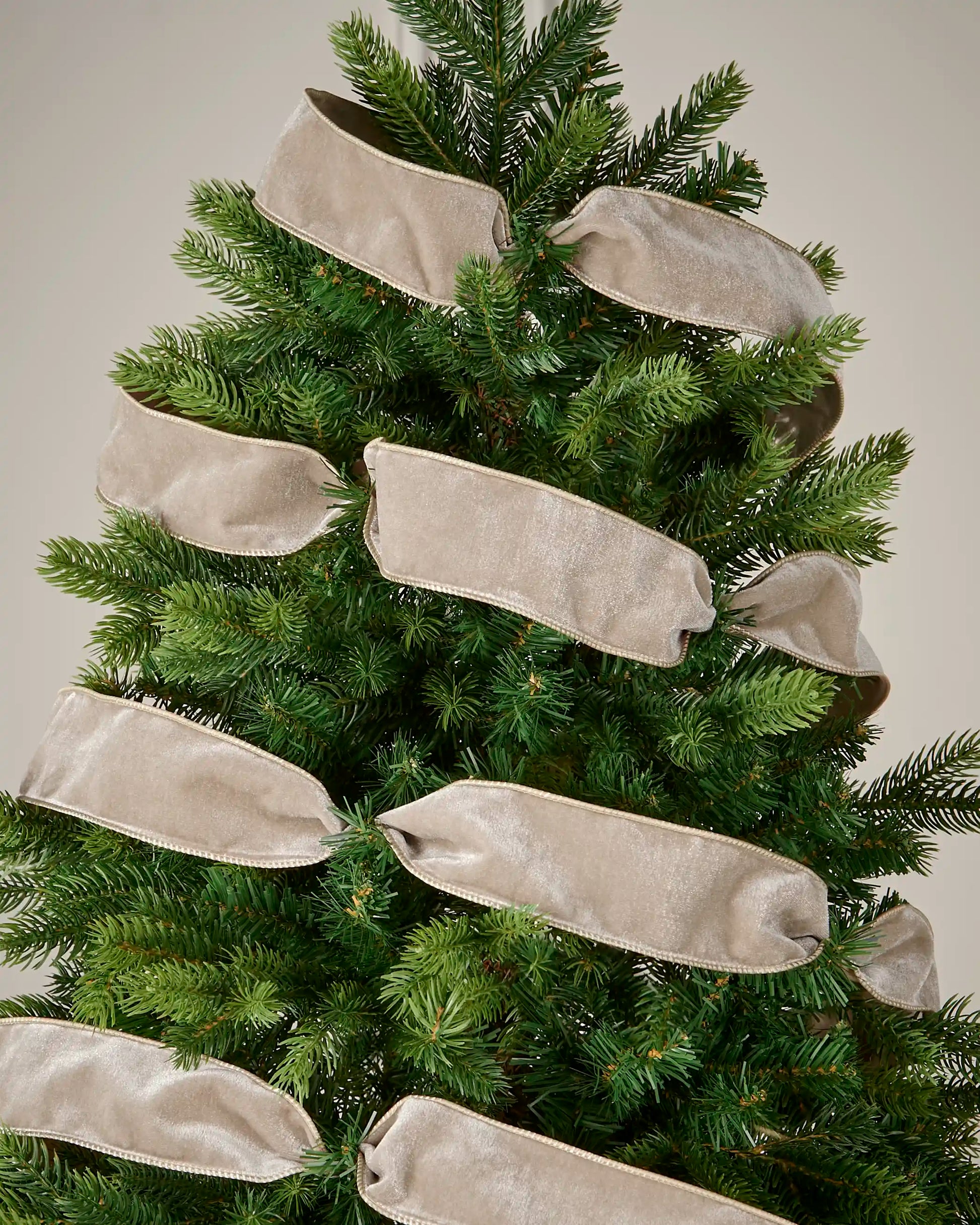 Latte wired velvet ribbon arranged around a Christmas tree for a soft neutral decorative finish.