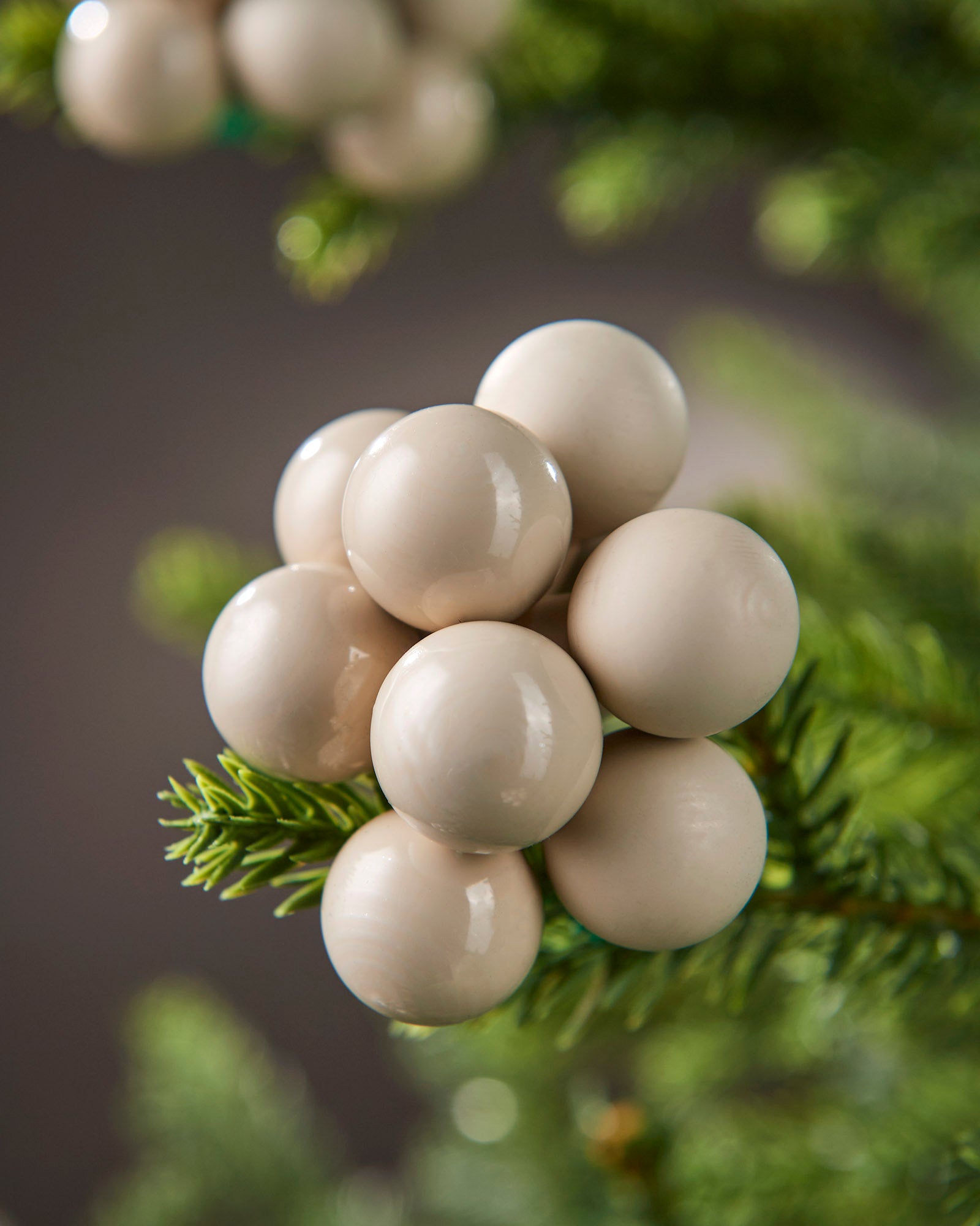 Detailed close-up of latte glass berry cluster baubles nestled among green tree branches.