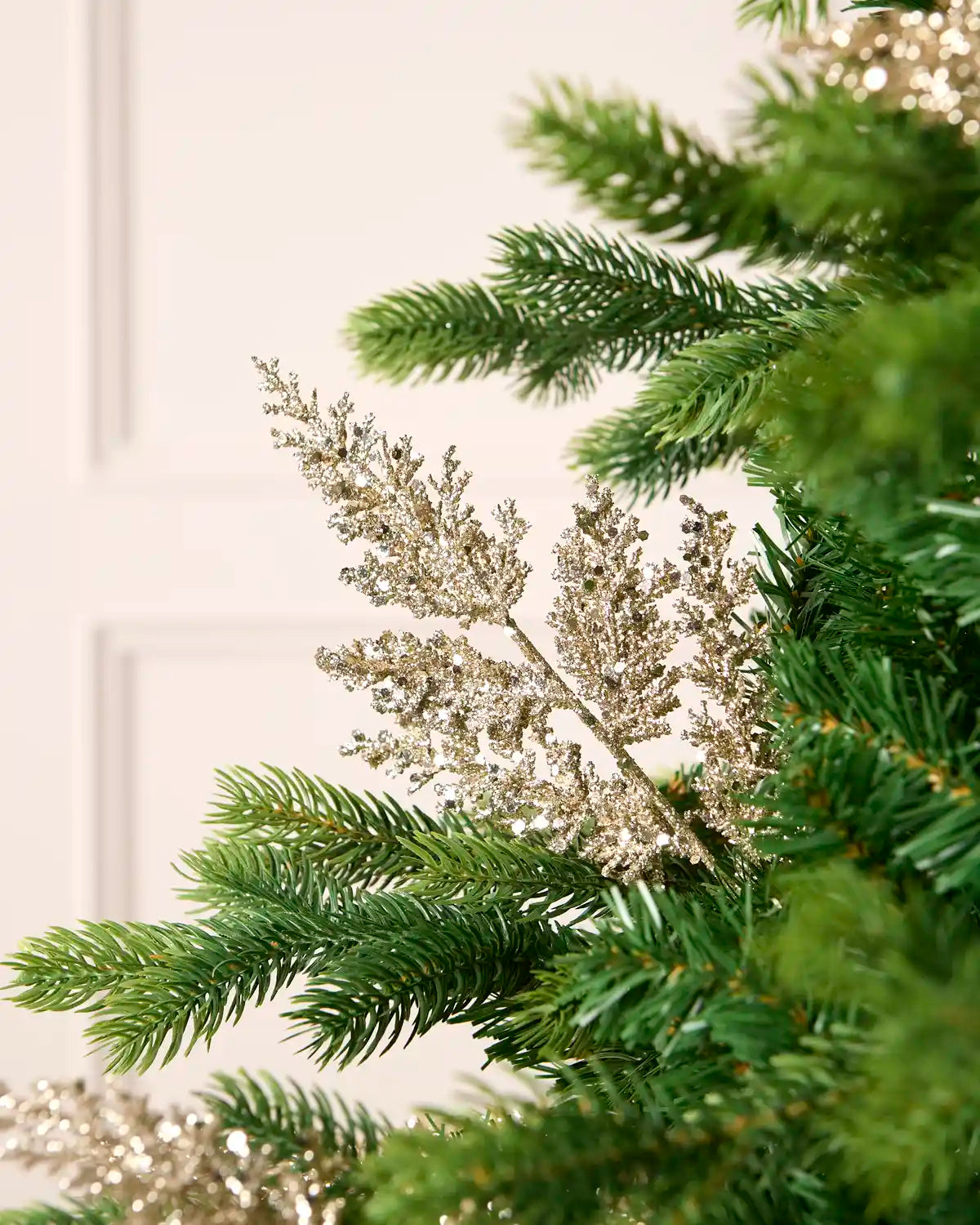 Latte glitter leaf pick arranged amongst green Christmas tree branches.