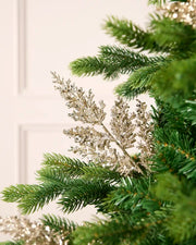 Latte glitter leaf pick arranged amongst green Christmas tree branches.