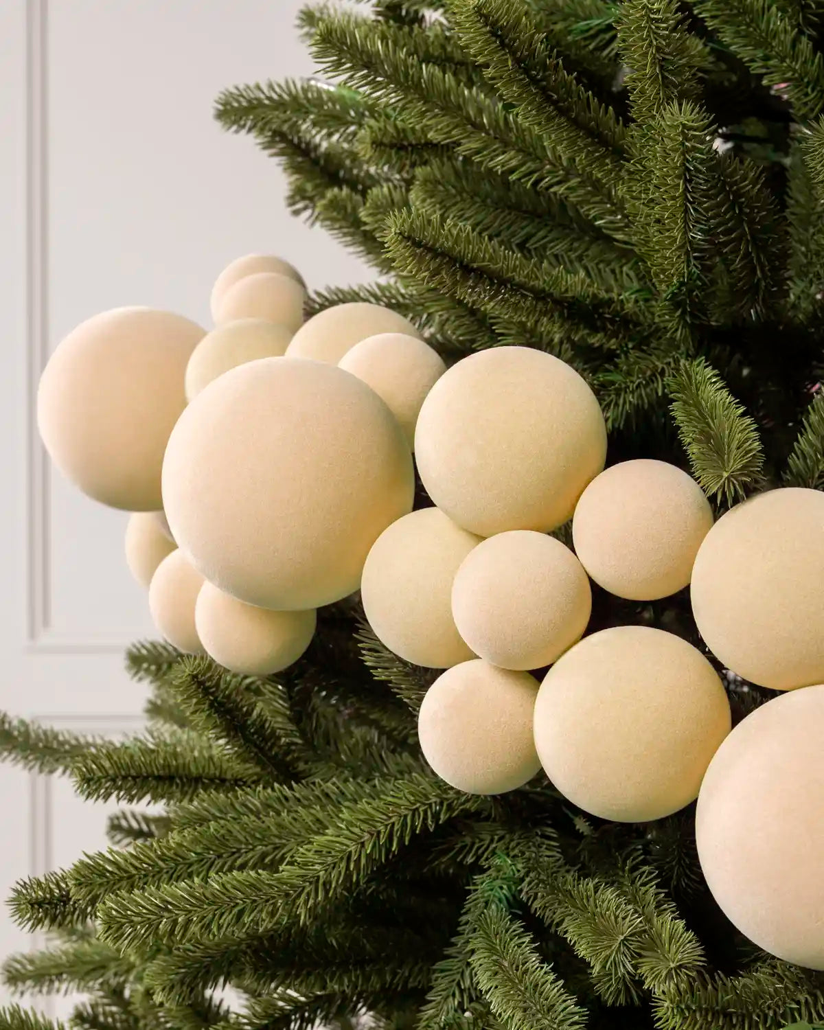 Close-up of latte velvet bauble garland on a Christmas tree showing the soft textured finish and mixed bauble sizes.