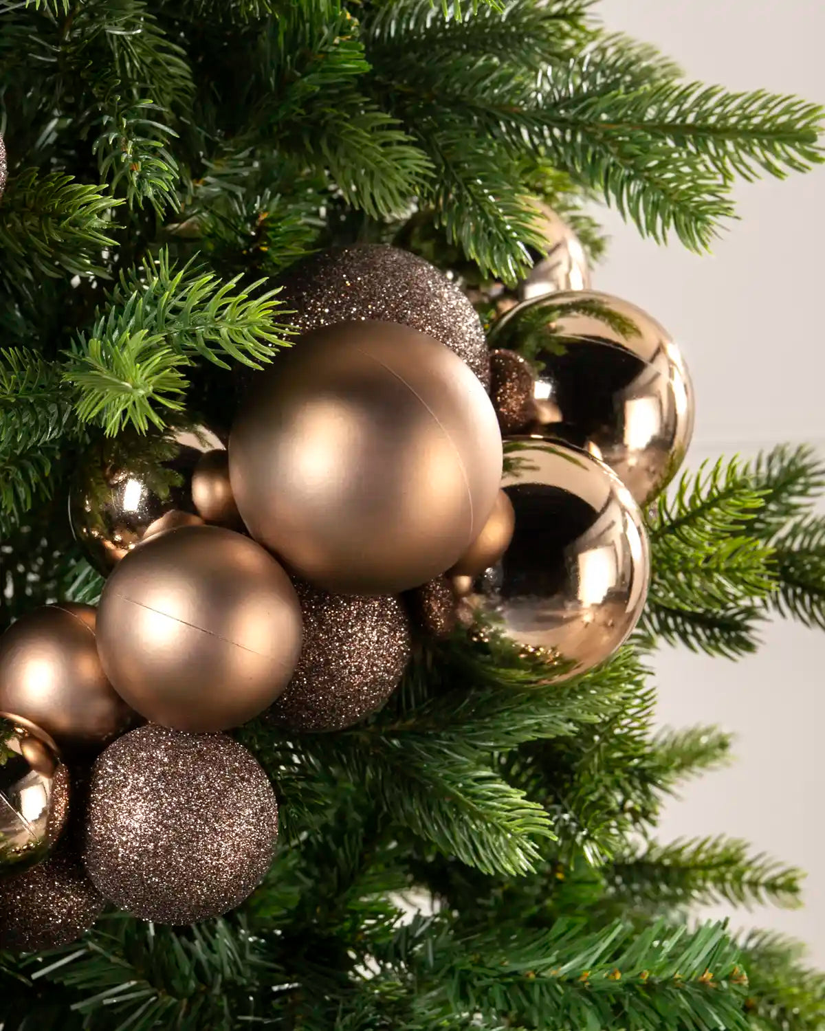Close-up of mocha baubles showing shiny, matt and glitter finishes against green Christmas tree branches.