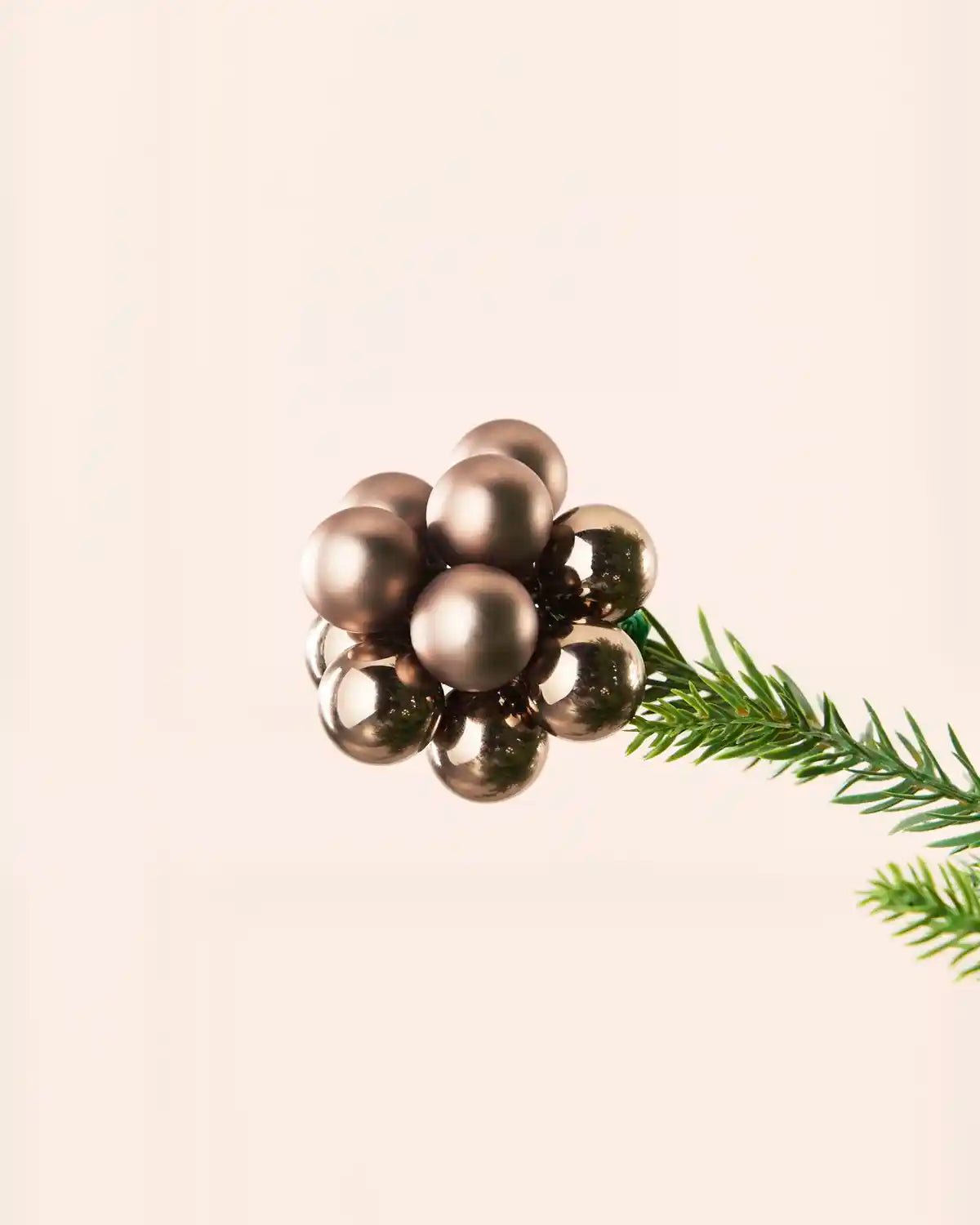 Close-up of a mocha glass berry cluster bauble attached to a Christmas tree branch.