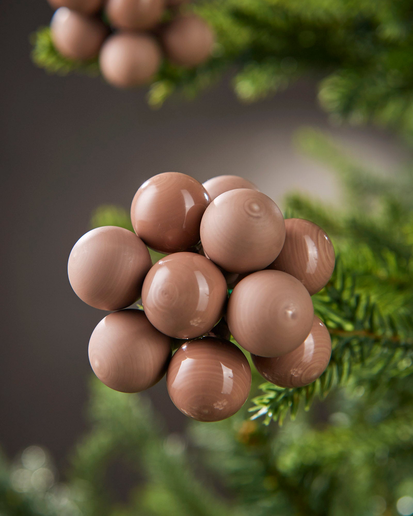 Detailed close-up of mocha glass berry cluster baubles nestled among green tree branches.