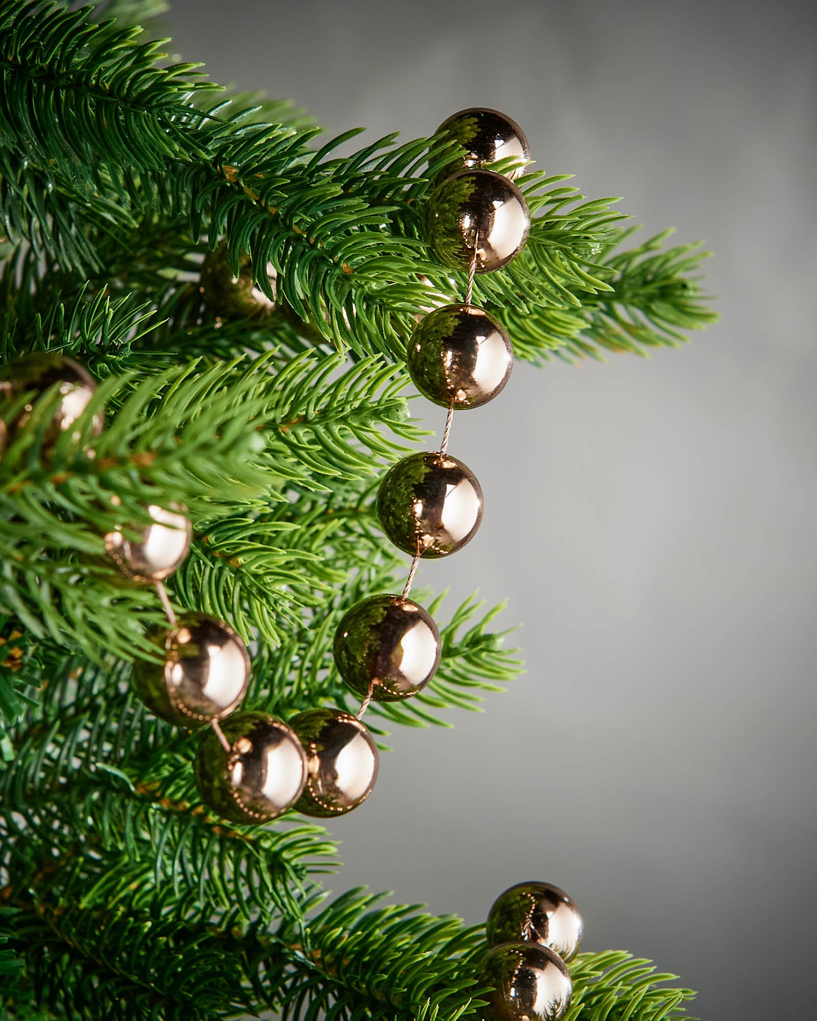 Mocha beaded garland hanging from green Christmas tree branches, showing the glossy bead finish.