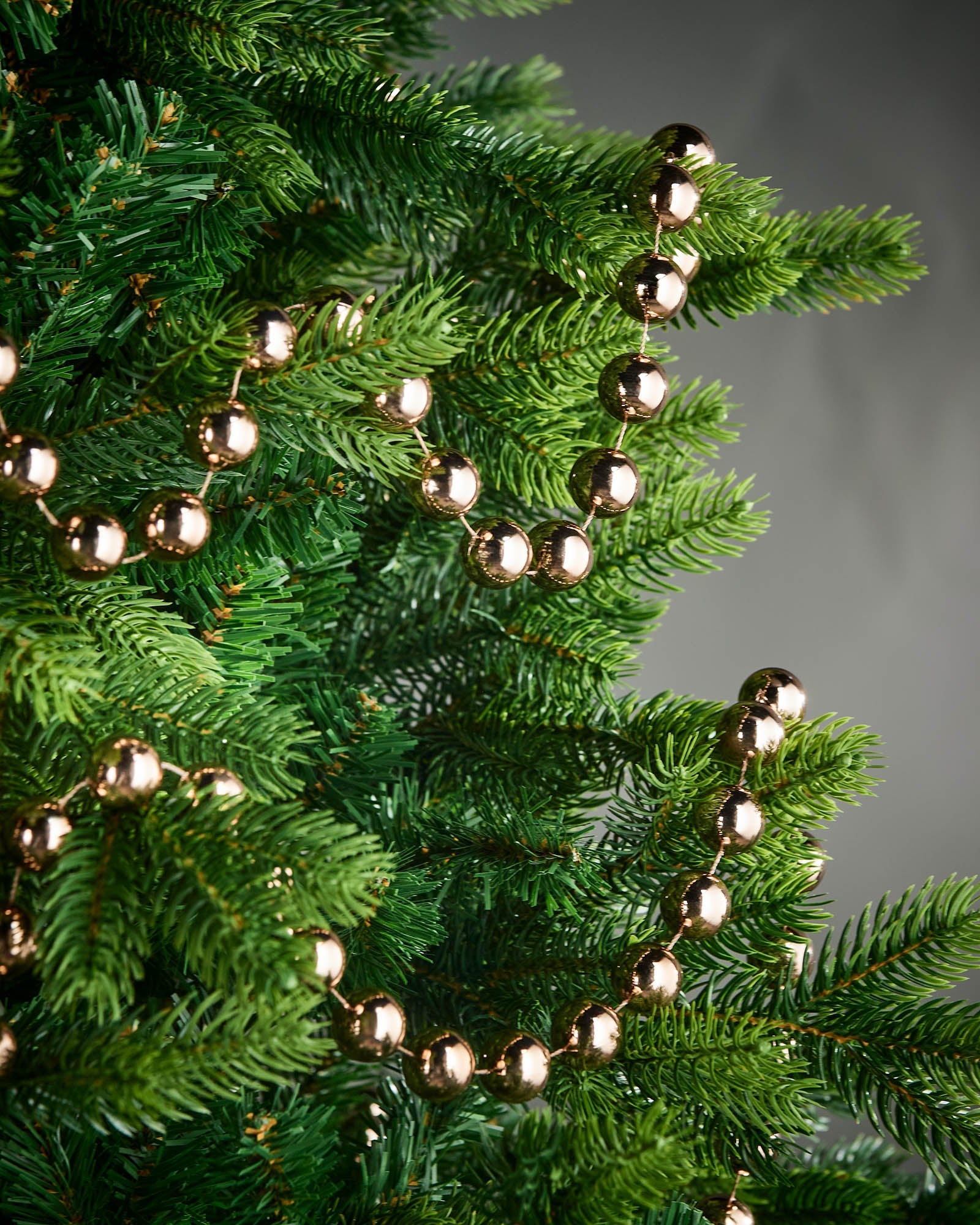 Mocha oversized beaded garland draped through green Christmas tree branches.