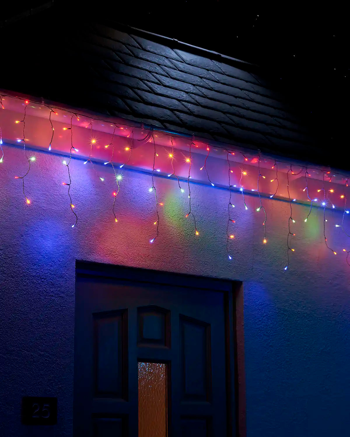 Multi-colour icicle lights with white cable displayed along a roofline above a front door at night.