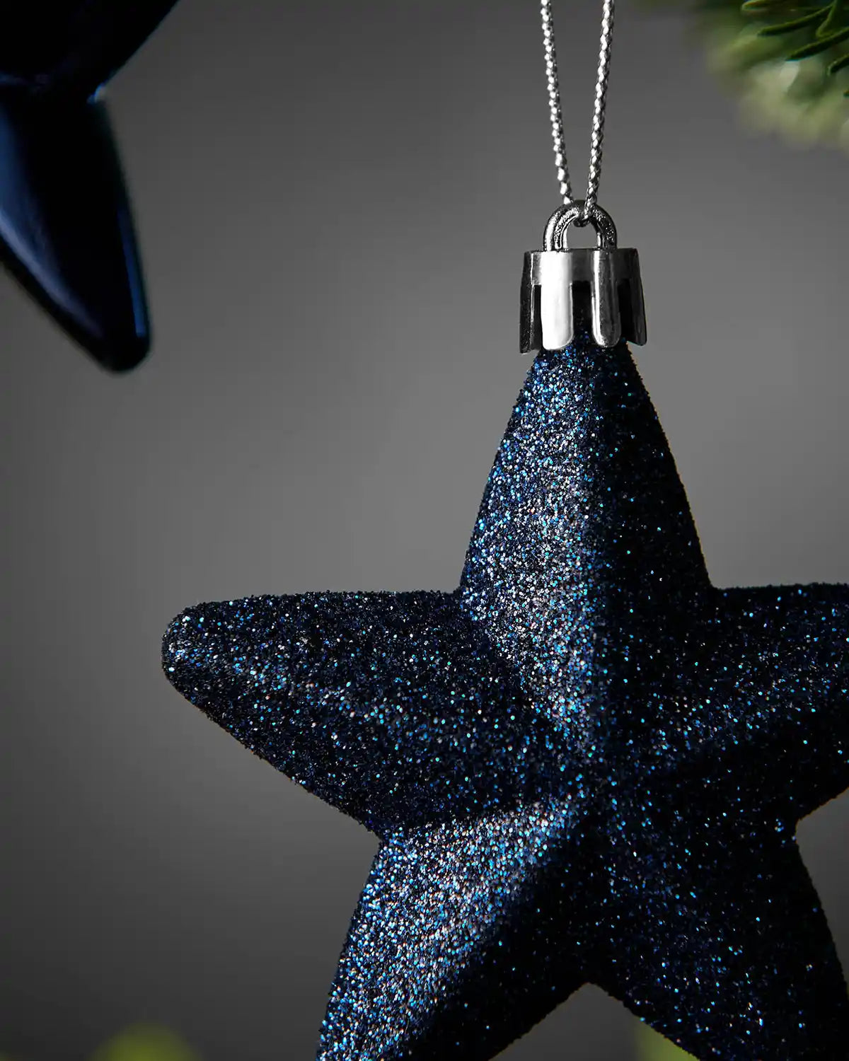 Close-up of a navy blue 7cm glitter hanging star with silver cap and string.