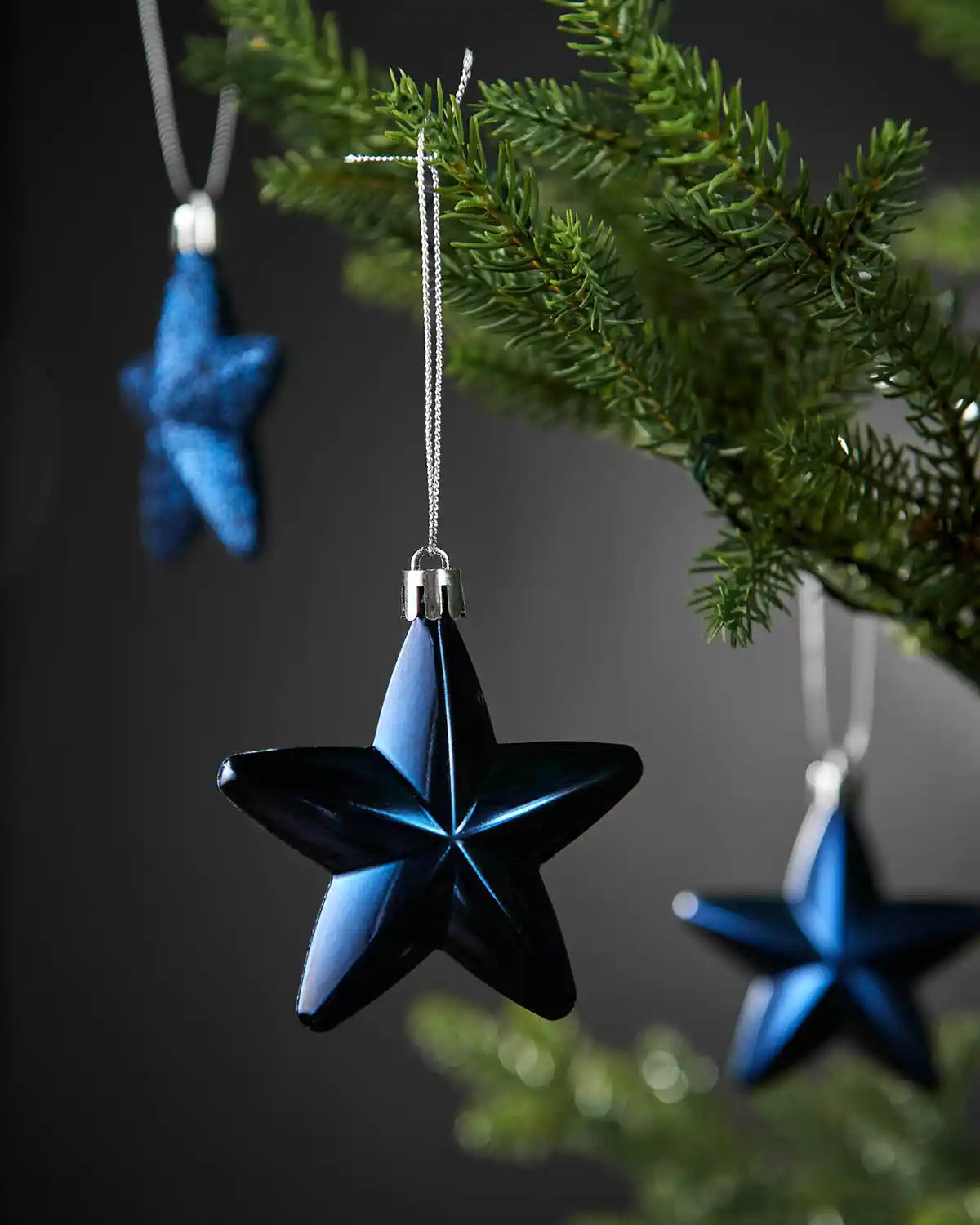 Close-up of a shiny navy blue 7cm hanging star with silver string on a Christmas tree.
