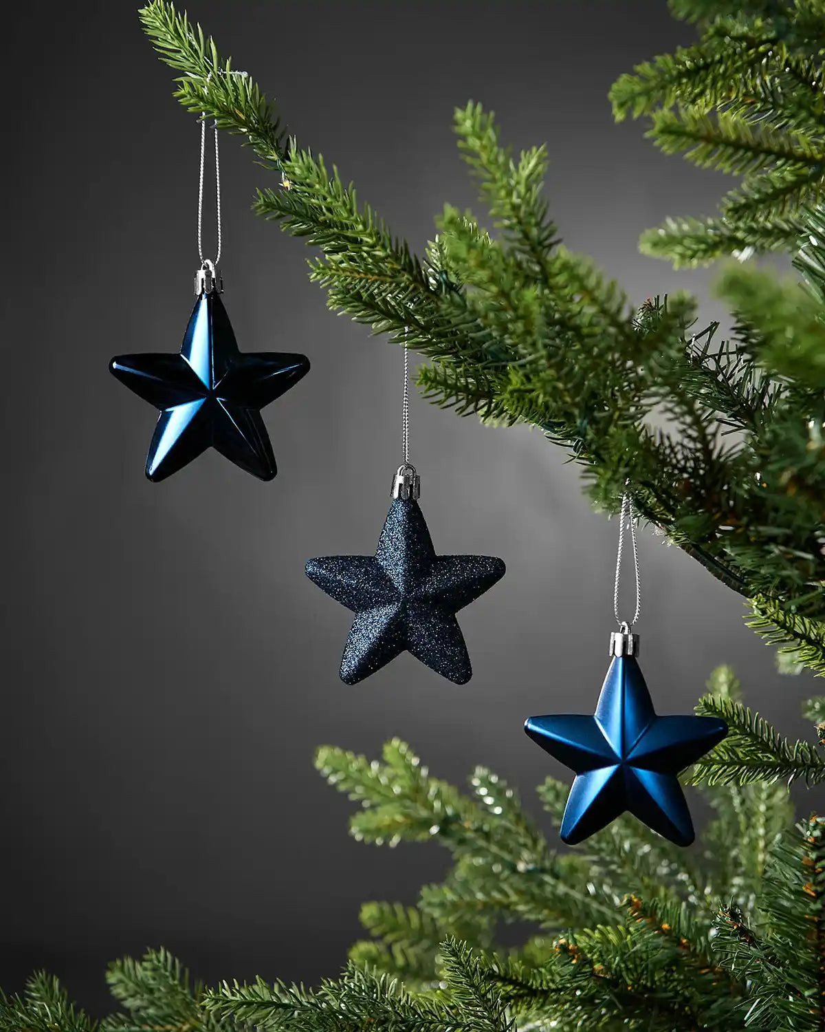 Navy blue 7cm hanging star decorations in shiny, glitter and matte finishes displayed on a Christmas tree.