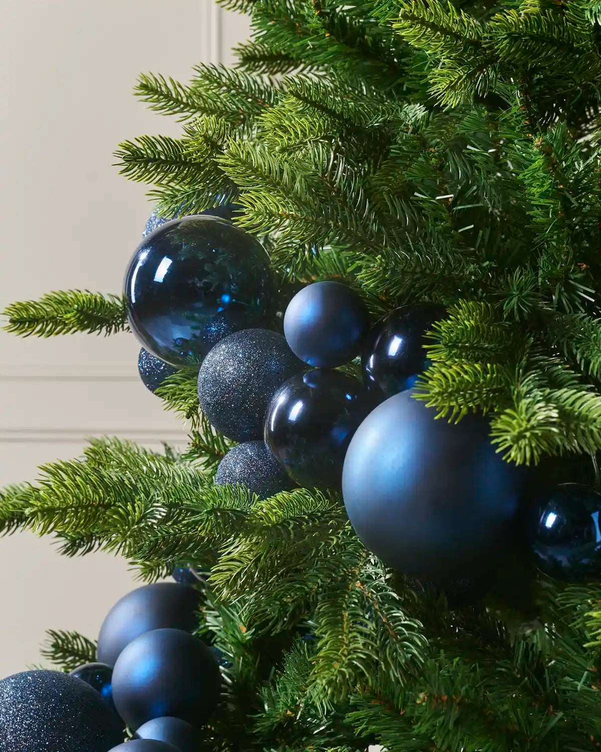 Close-up of navy blue bauble garland on a Christmas tree showing mixed sizes and finishes.