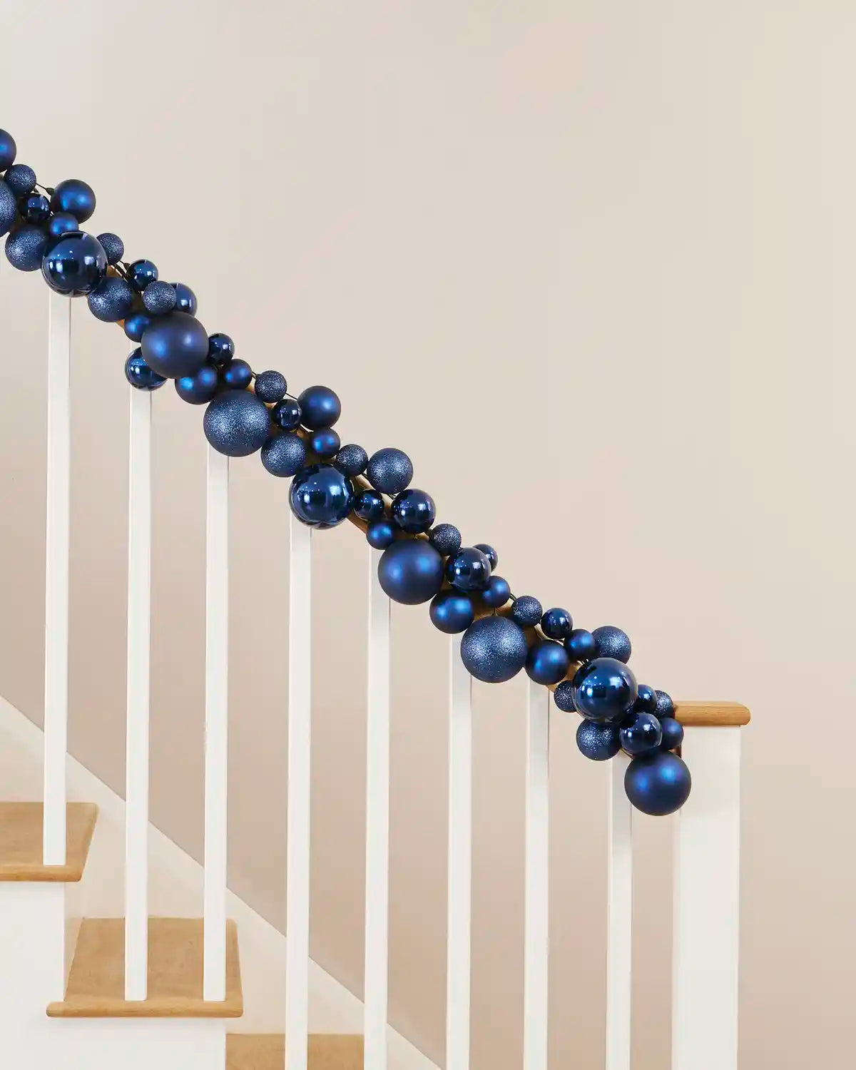 Navy blue bauble garland arranged along a staircase handrail with varied bauble sizes and finishes.