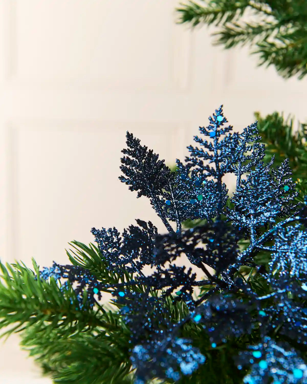 Navy glitter leaf picks displayed across green Christmas tree branches with reflective blue details.