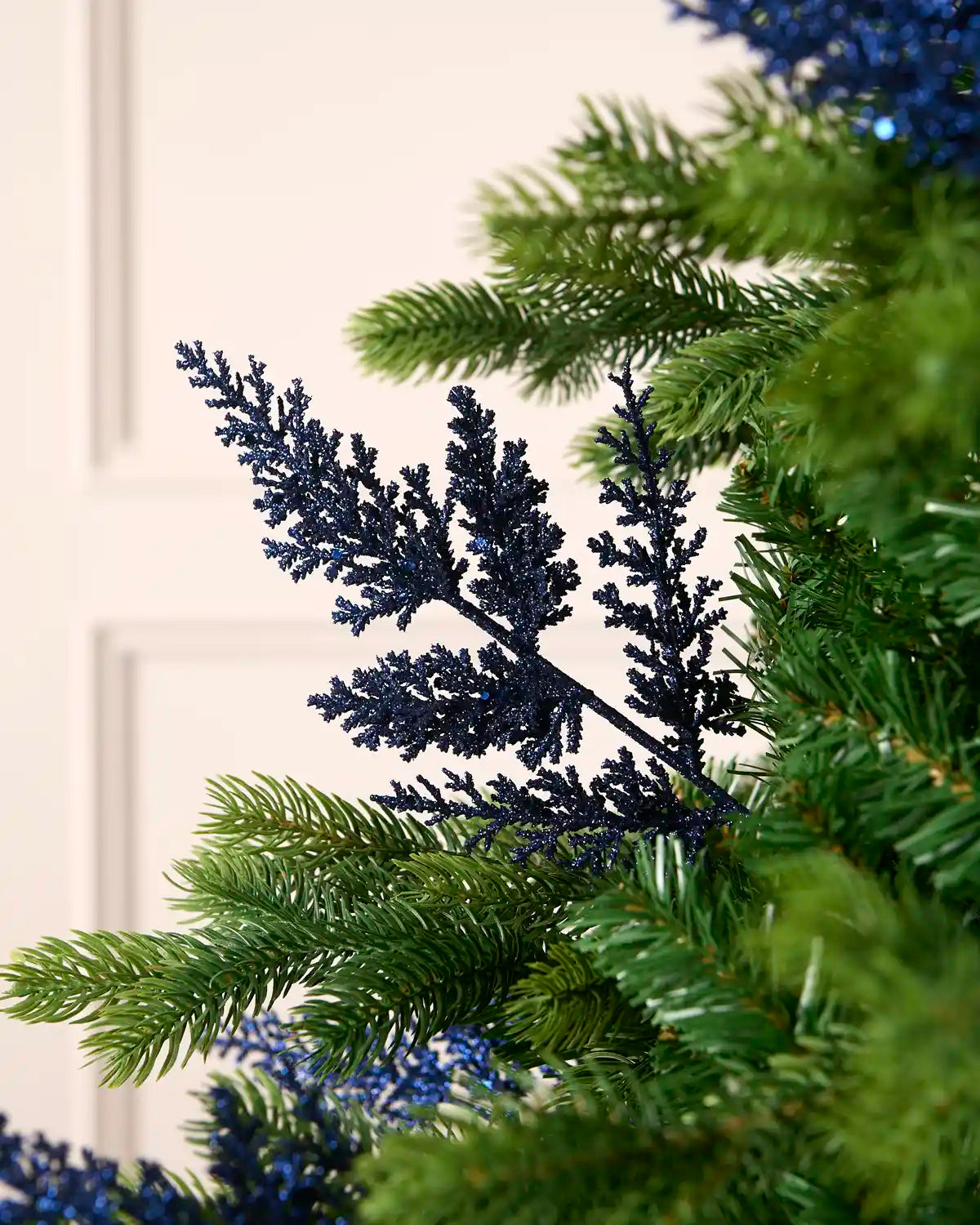 Navy glitter leaf pick arranged amongst green Christmas tree branches.