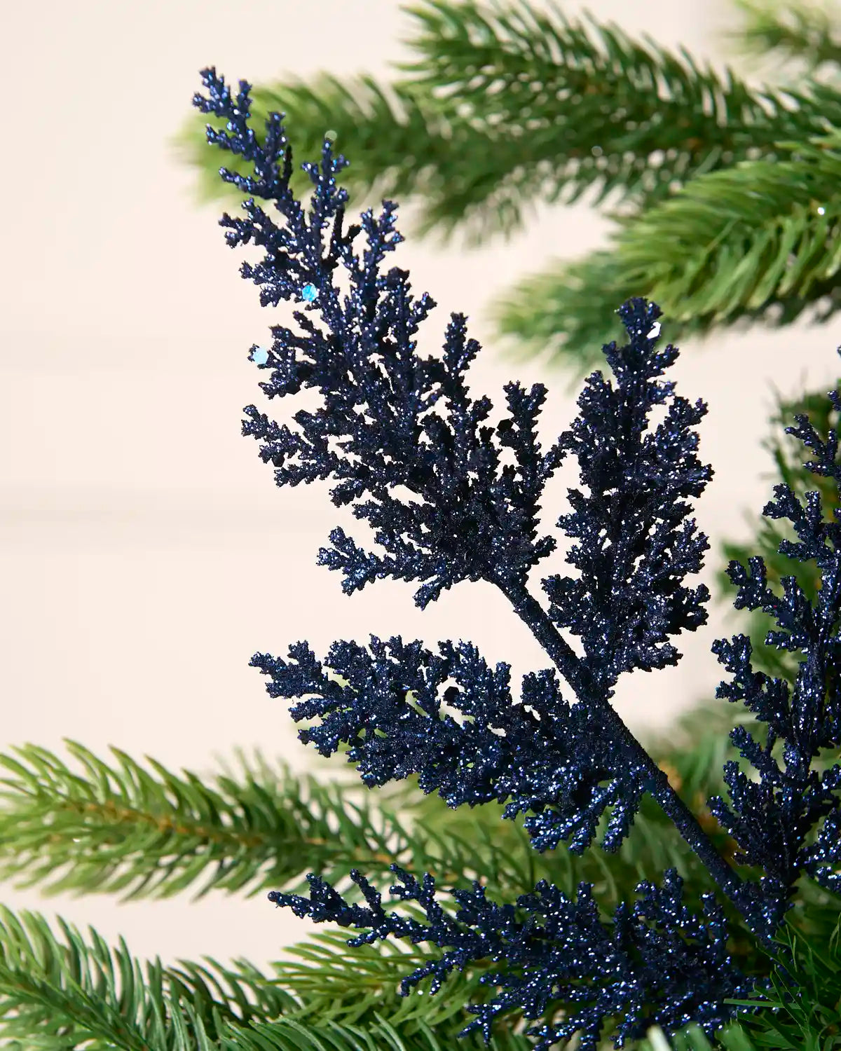 Navy glitter leaf pick with branched foliage displayed amongst Christmas tree greenery.