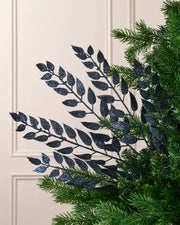 Navy leaf Christmas tree spray arranged among green Christmas tree branches.