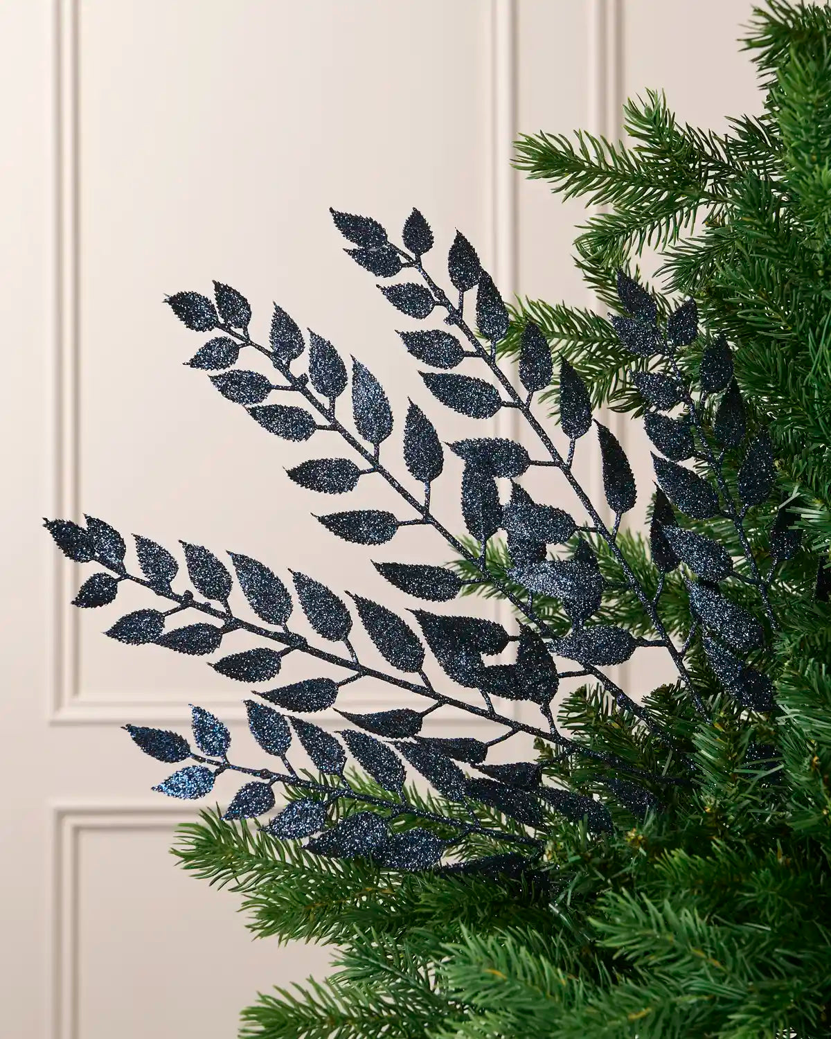 Navy leaf Christmas tree spray arranged among green Christmas tree branches.