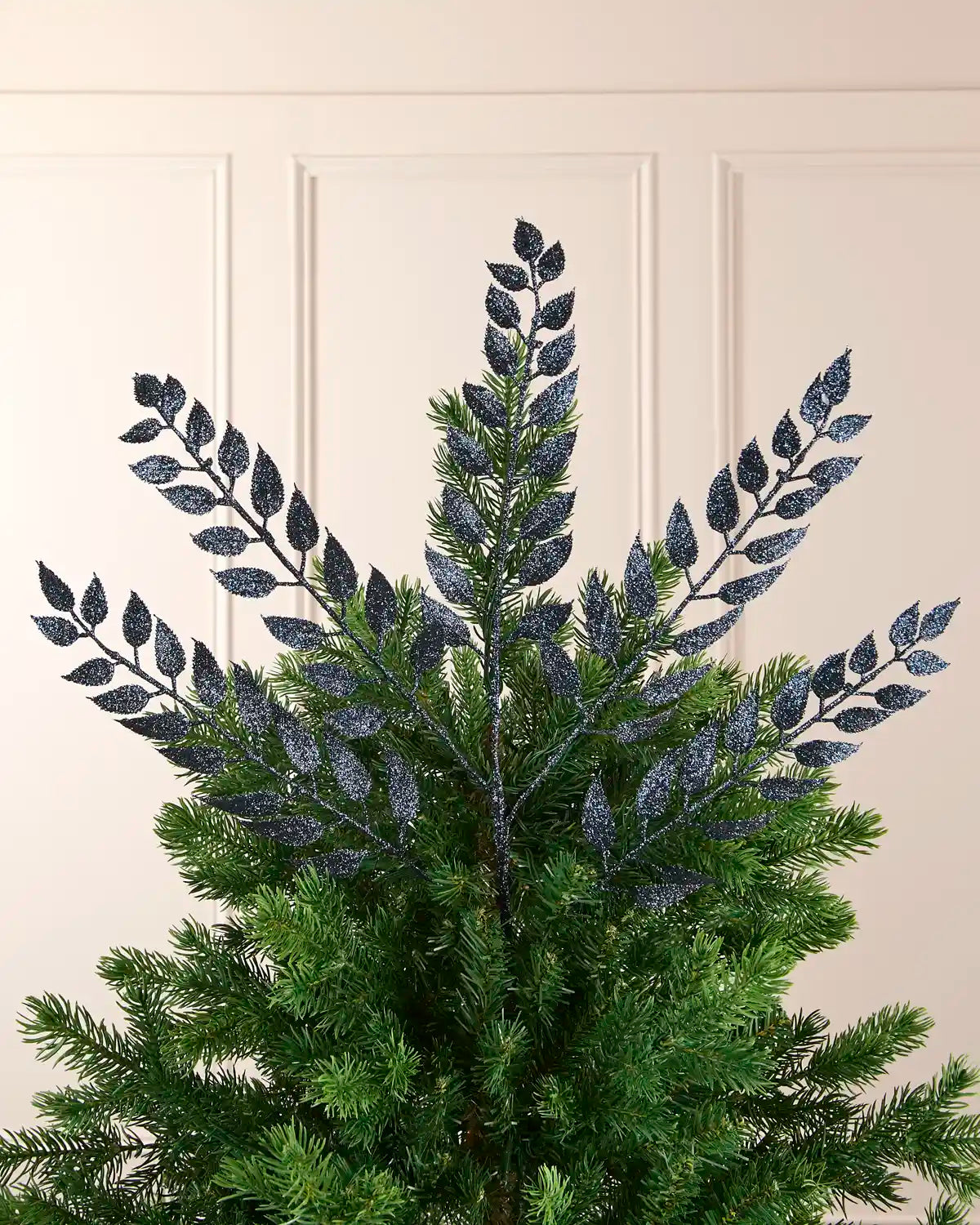 Navy leaf Christmas tree spray styled at the top of a green Christmas tree.
