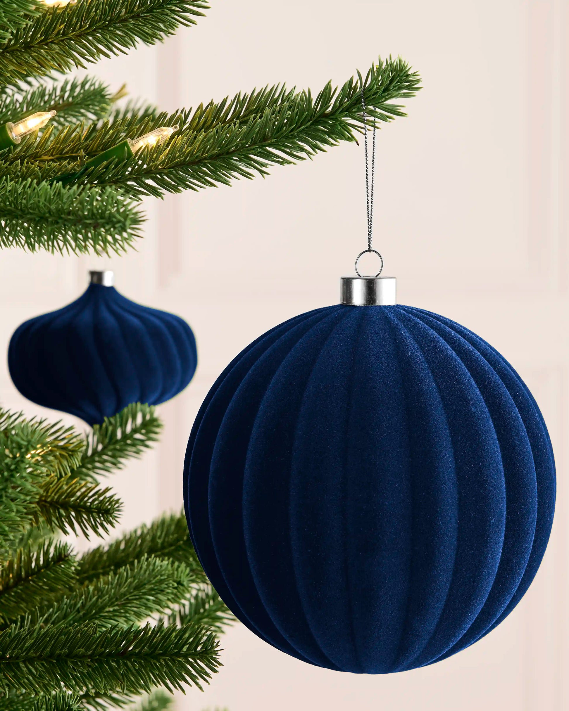 Navy 15 cm ribbed velvet bauble hanging from a Christmas tree, with a matching spiral bauble visible behind.