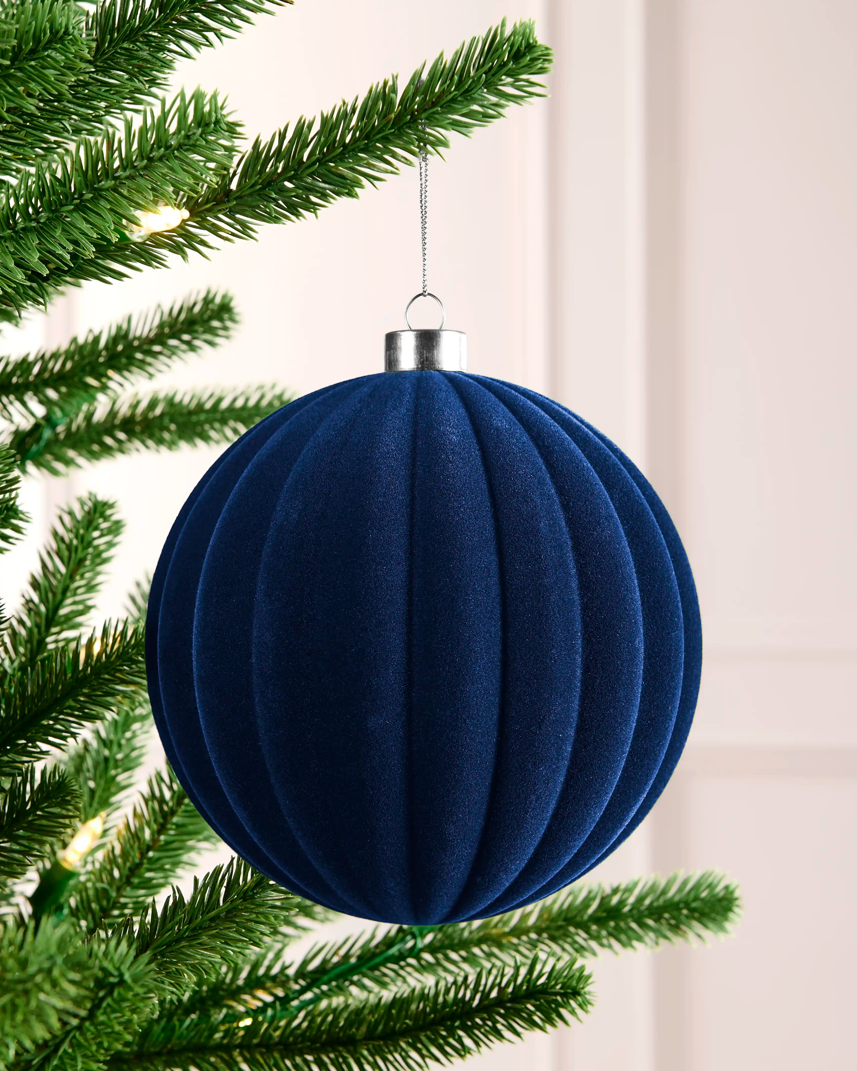 Navy 15 cm oversized velvet bauble with a ribbed round design, silver cap and hanging string on a Christmas tree.