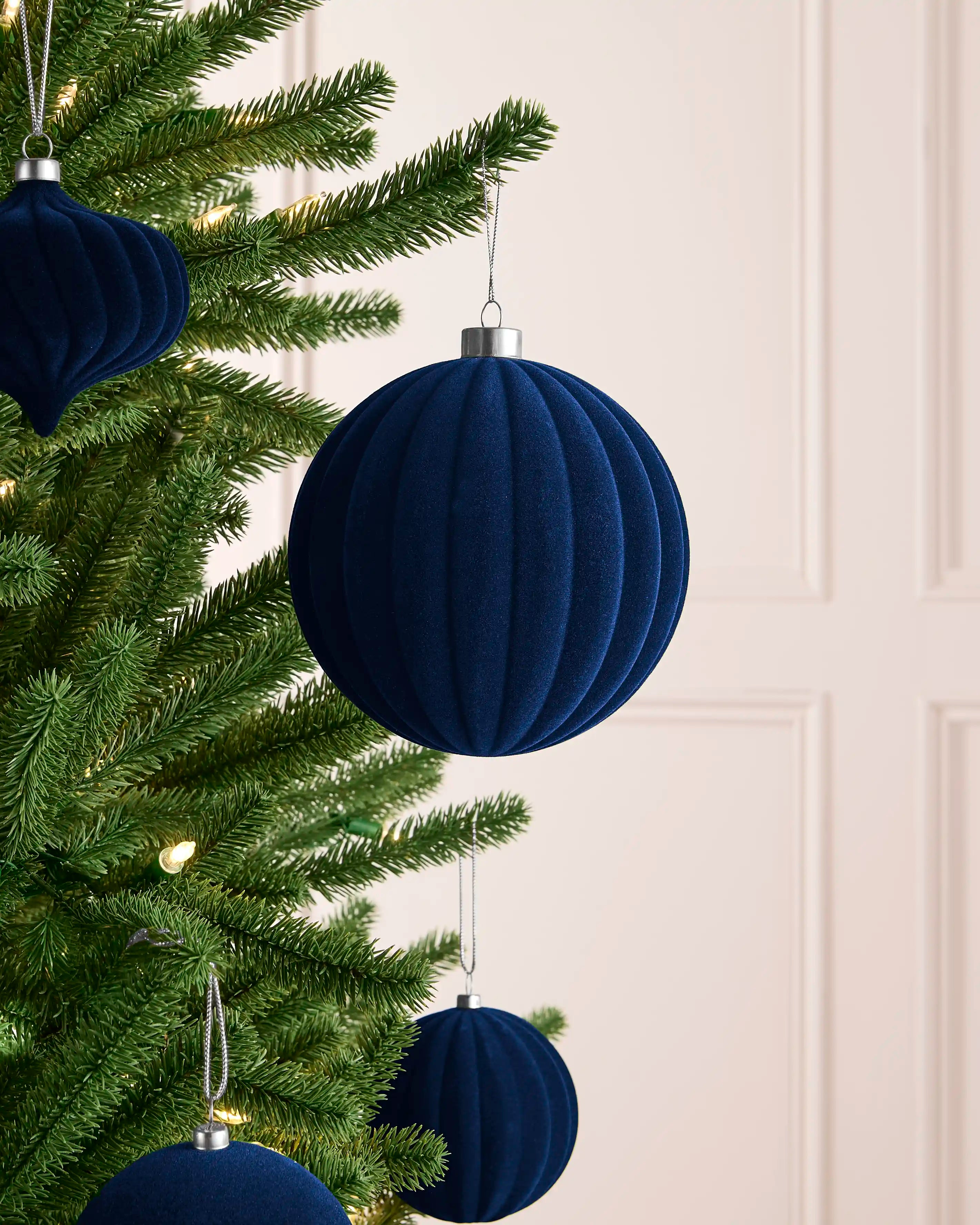 Navy 15 cm oversized ribbed velvet bauble displayed among matching navy decorations on a Christmas tree.