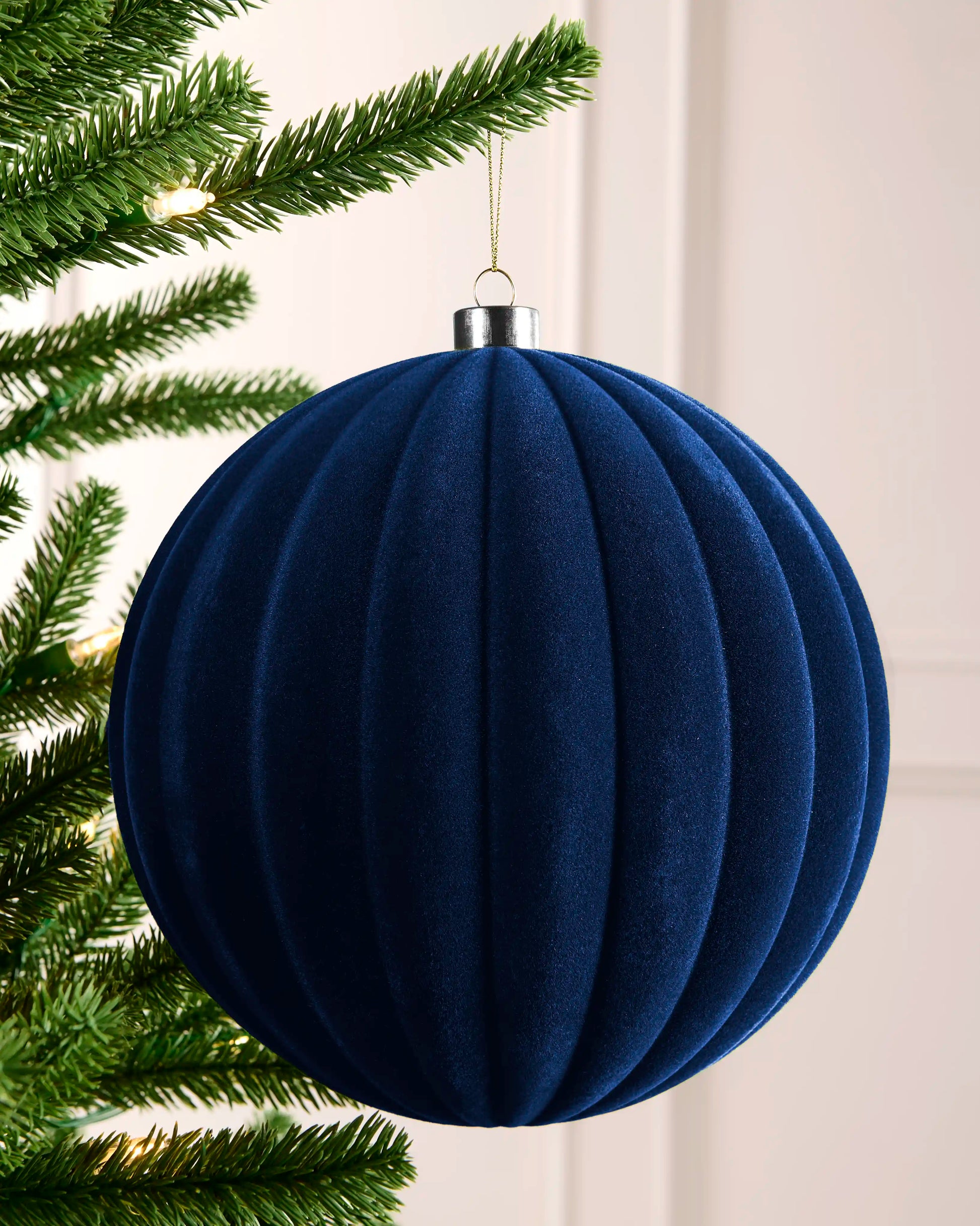 20 cm navy oversized velvet ribbed bauble hanging from a Christmas tree with a silver cap.