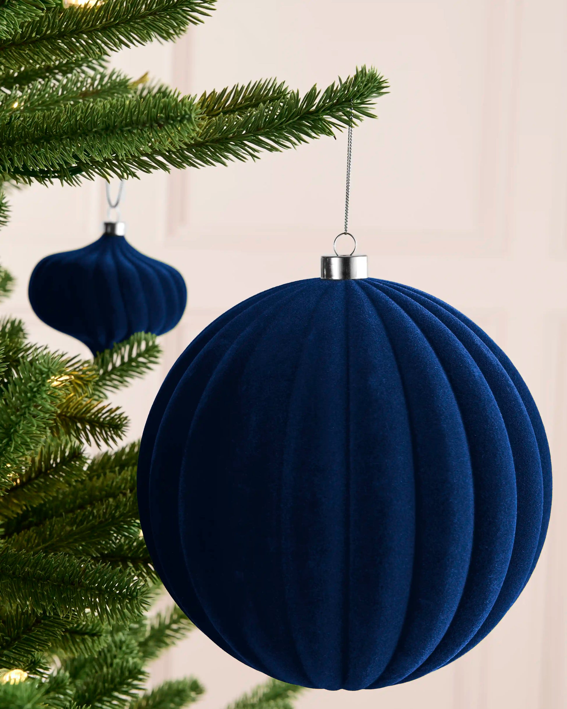 Navy 20 cm oversized velvet ribbed bauble displayed on a Christmas tree with silver hanging string.