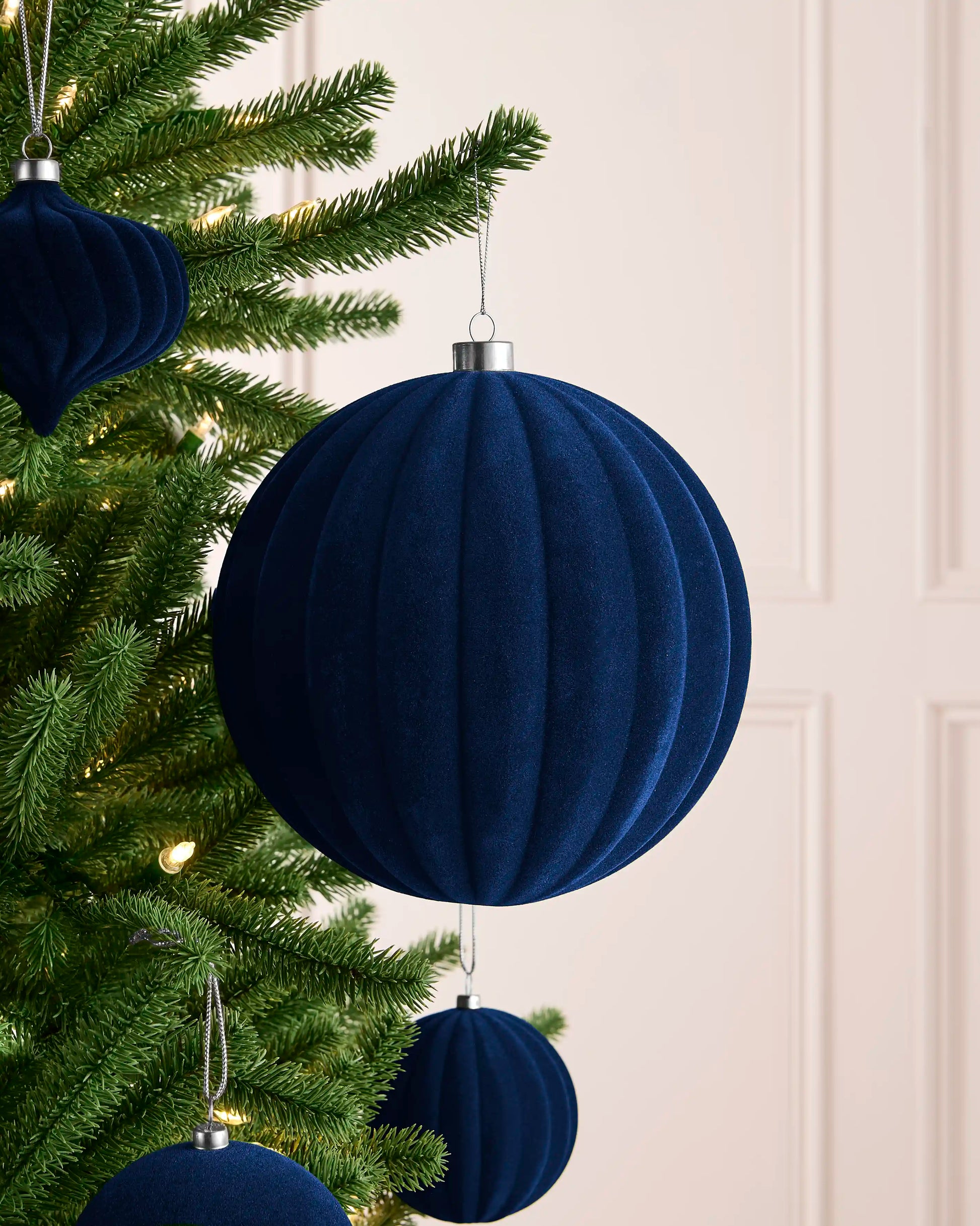 Oversized 20 cm navy velvet ribbed bauble styled on a Christmas tree with coordinating navy ornaments.