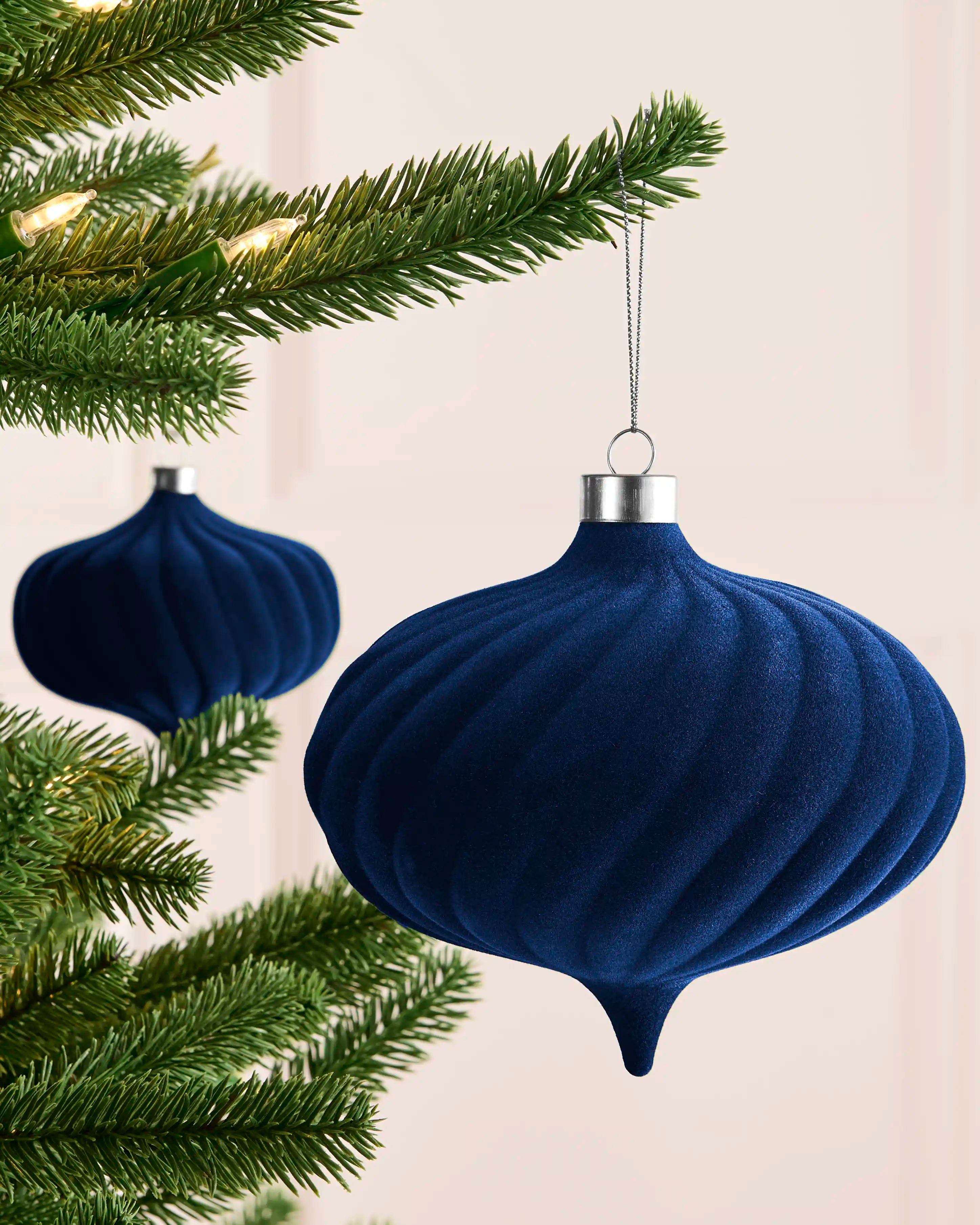 Navy 15 cm spiral velvet bauble hanging from a Christmas tree, showing its curved textured profile and pointed base.