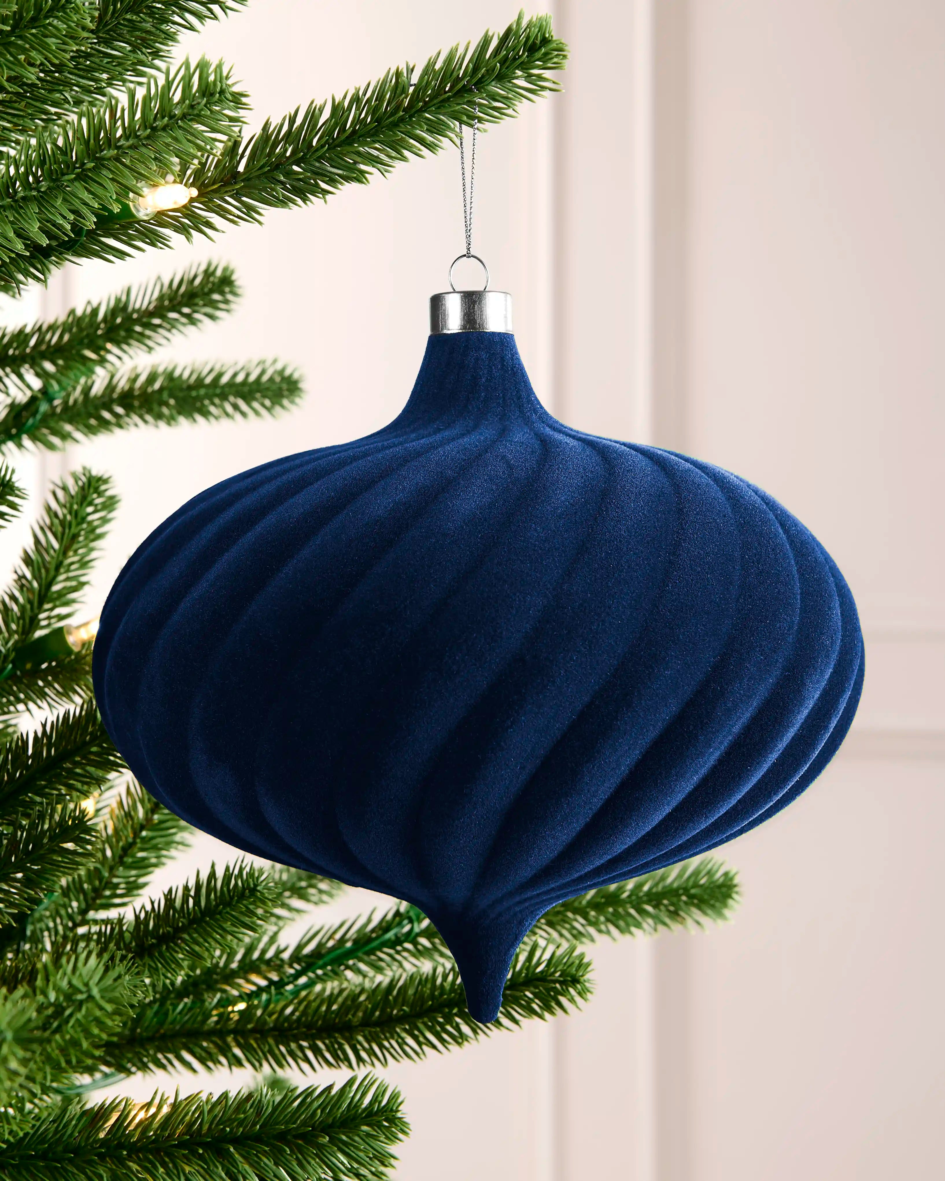 Navy 20 cm oversized velvet bauble with spiral detailing, silver cap and hanging string on a Christmas tree.