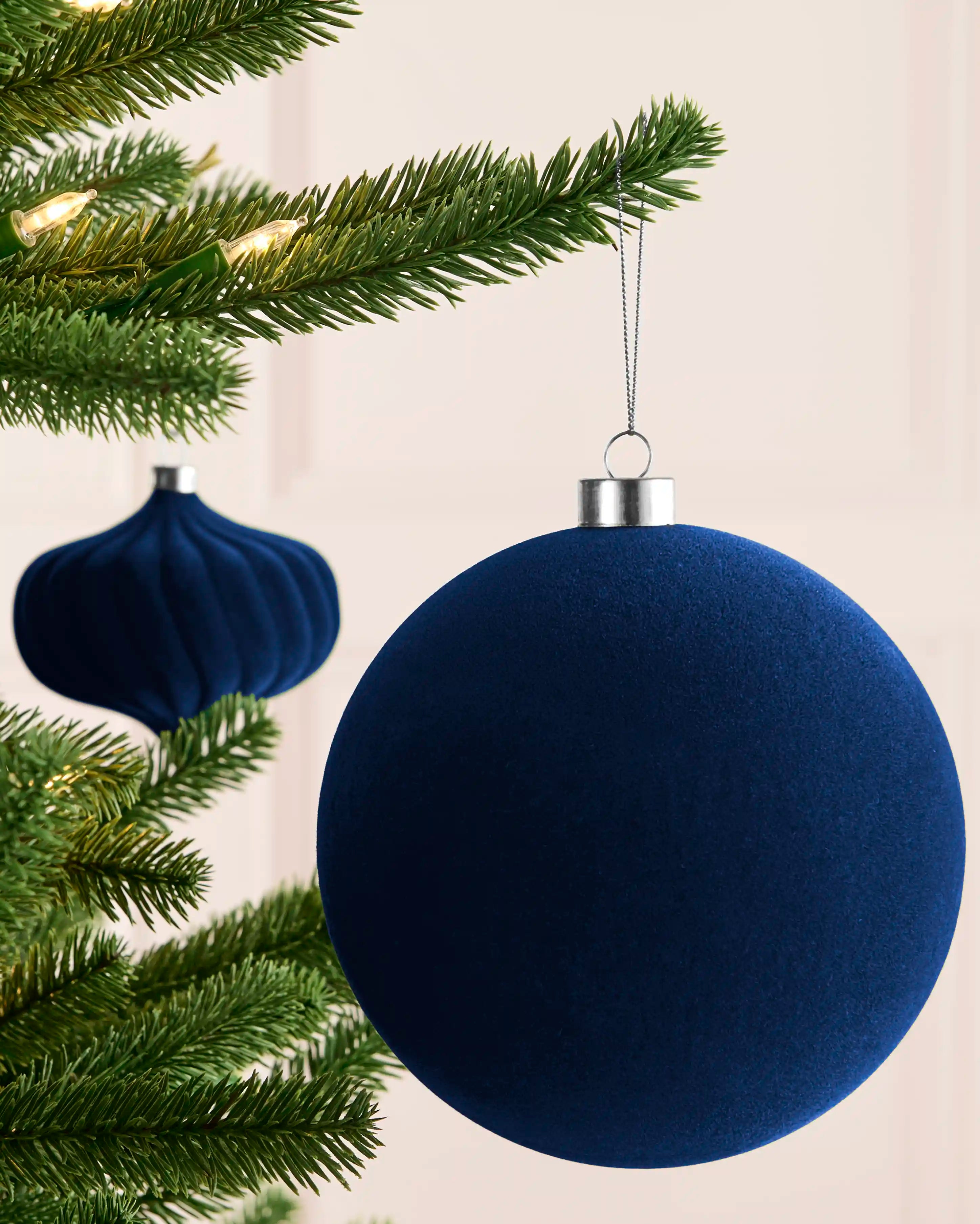 Navy 15 cm oversized velvet traditional bauble displayed on a Christmas tree with a matching navy bauble in the background.