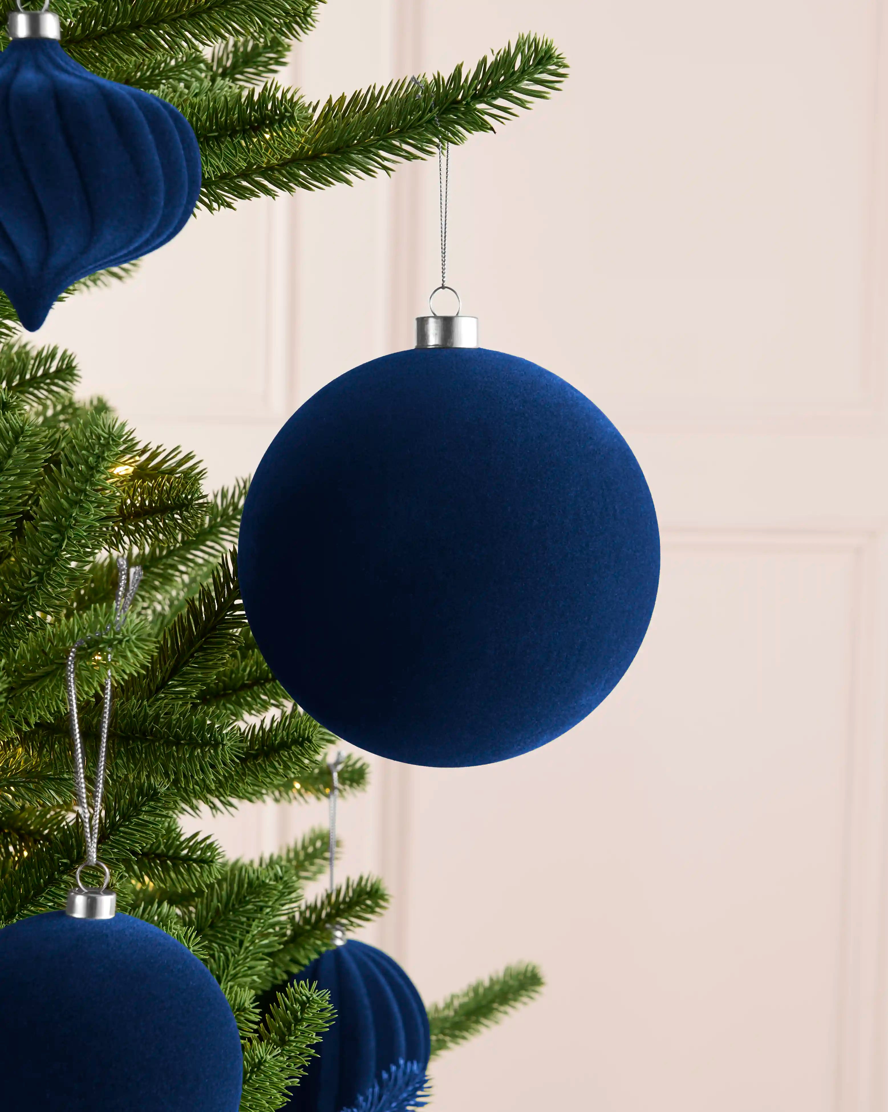 Large navy 15 cm oversized velvet traditional bauble styled on a Christmas tree with coordinating navy ornaments.