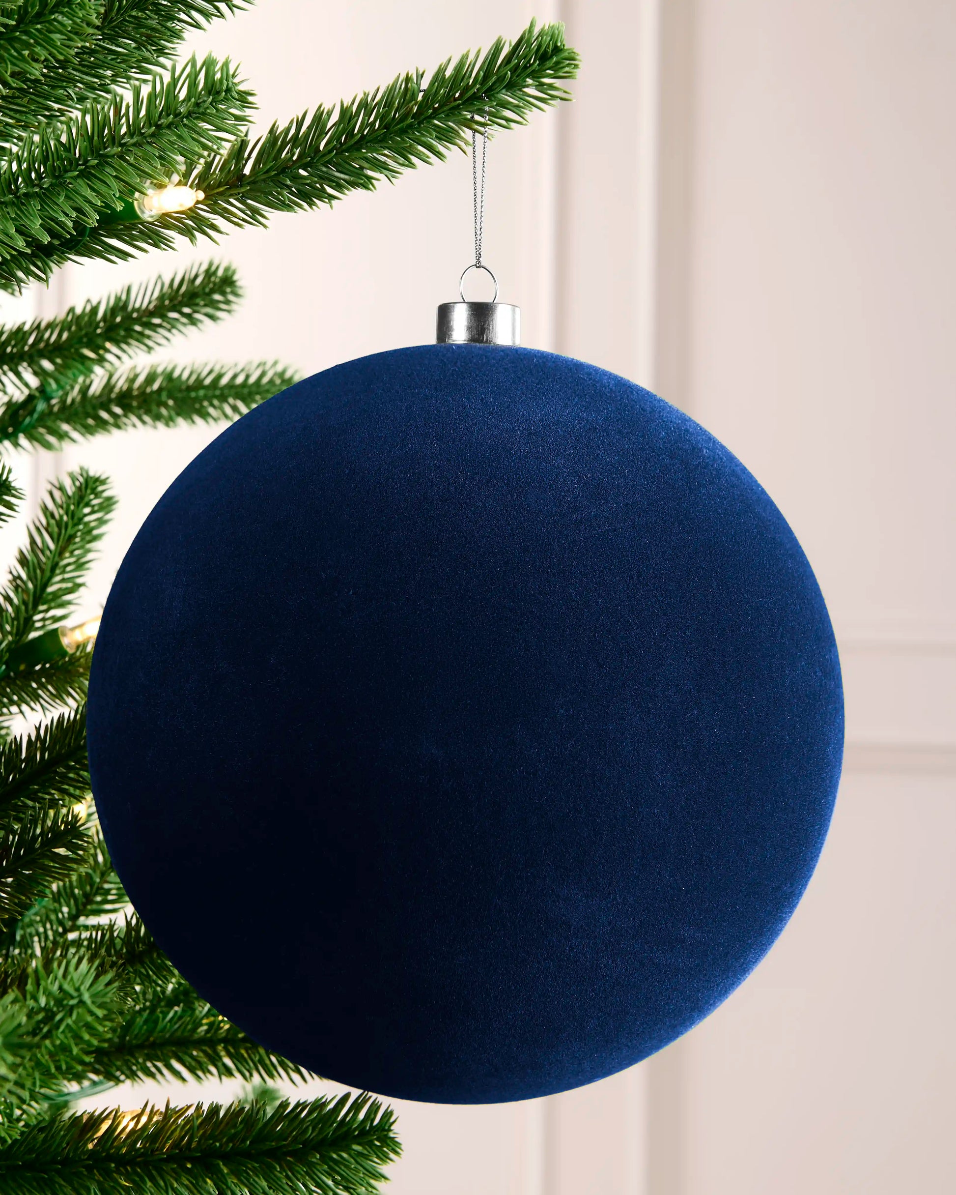 20 cm navy oversized velvet traditional bauble hanging on a Christmas tree with a silver cap and hanging string.